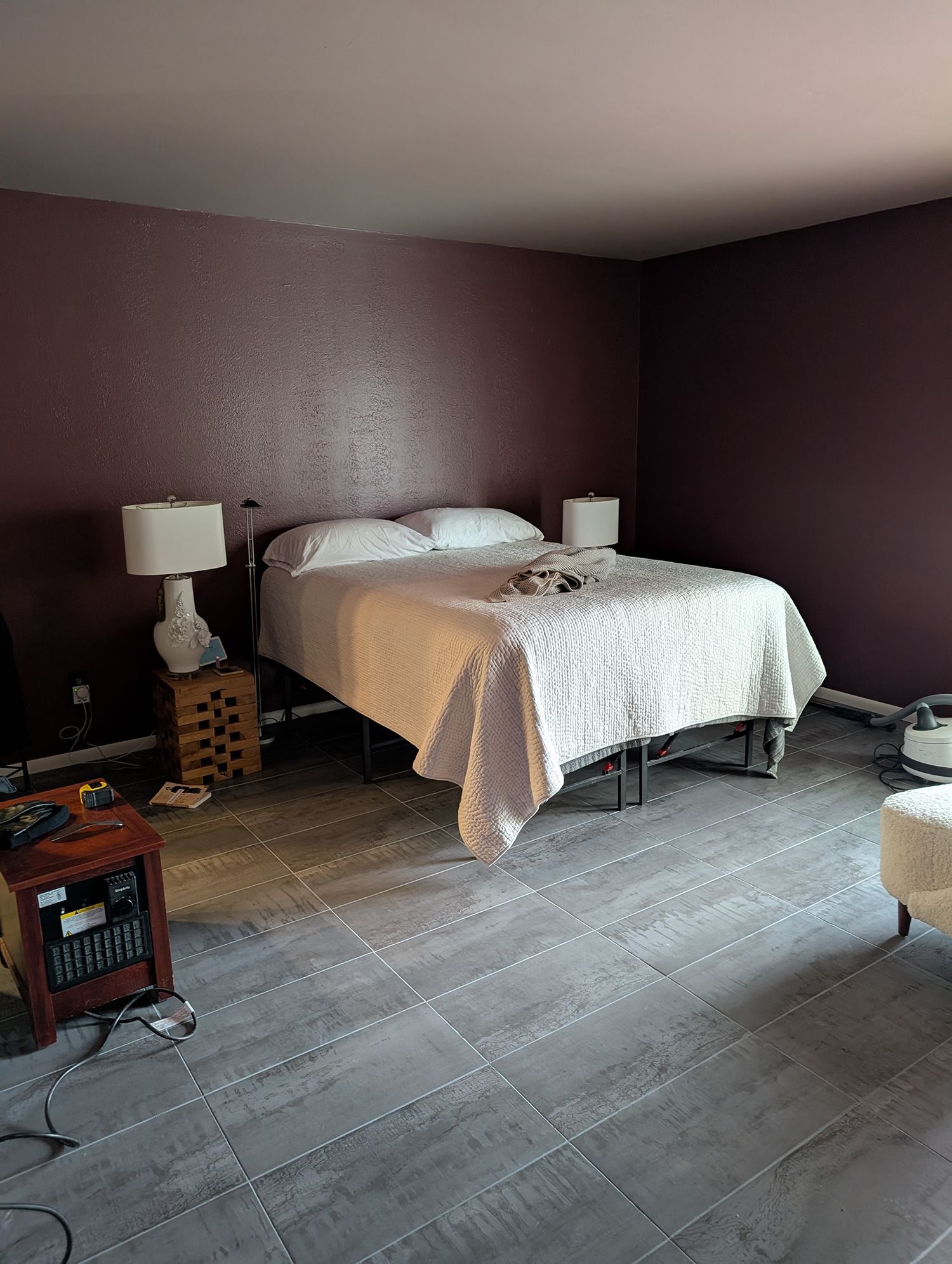 Bedroom with a bed, lamps, and dark purple walls. Gray tiled floor.