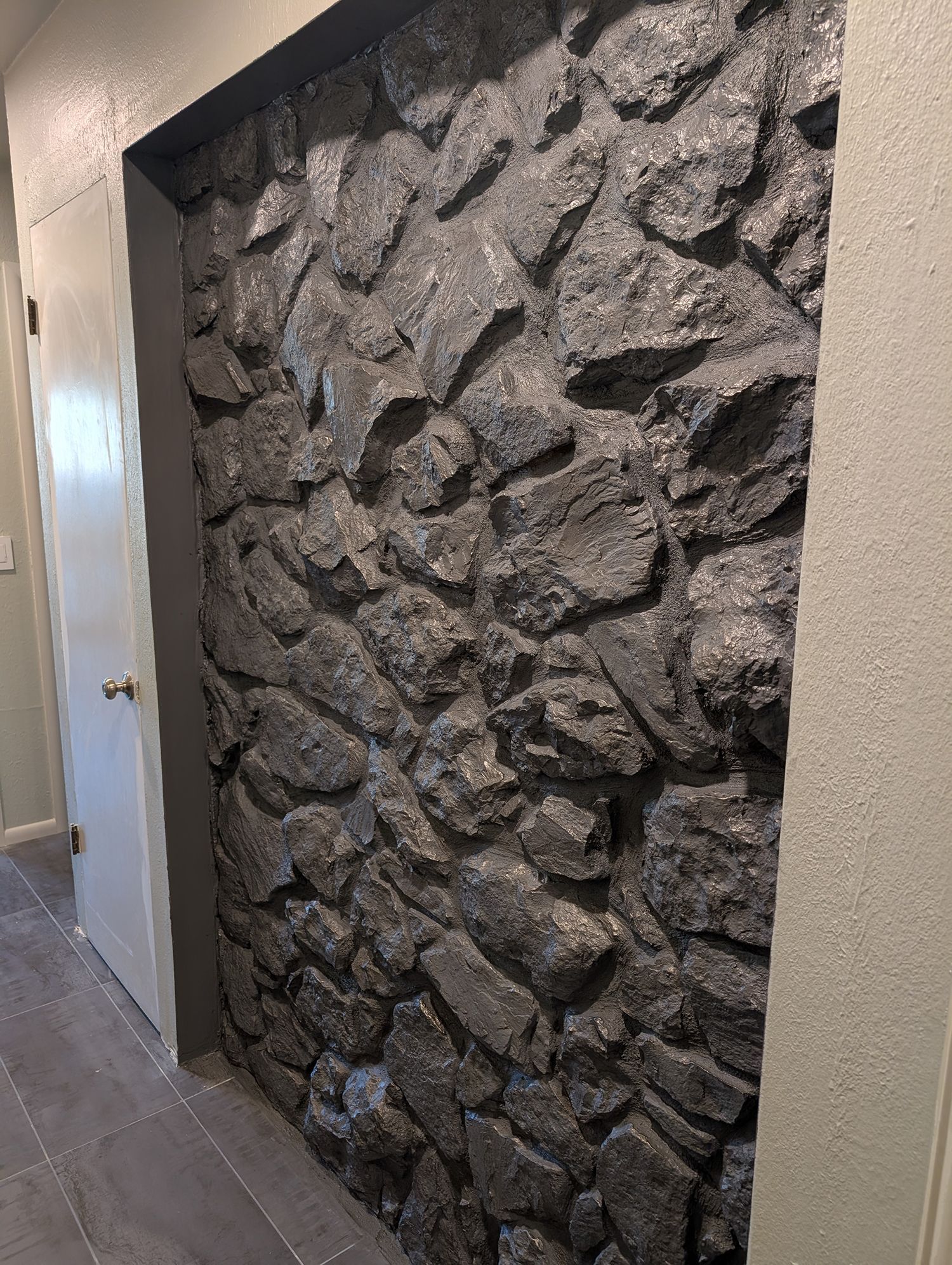 Stone accent wall with dark gray rocks, framed by gray and white walls, next to a white door.