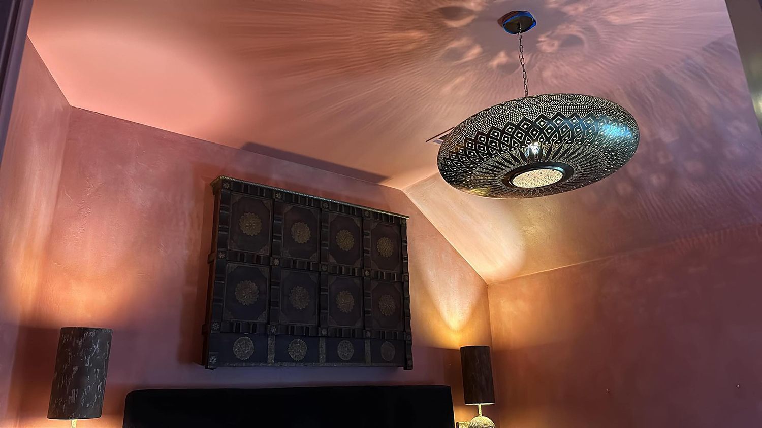 Bedroom with patterned, metallic light fixture and decorative wall panel; warm lighting.