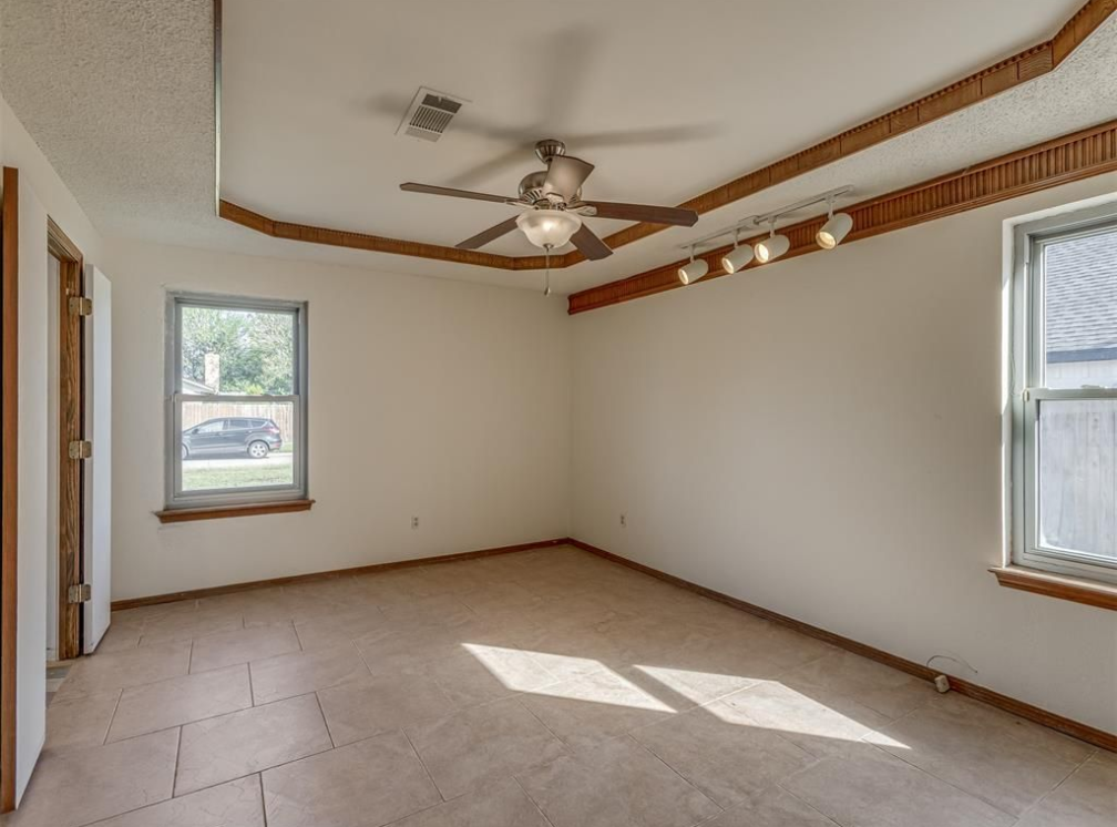 Empty room with windows, ceiling fan, and trim. Beige walls and carpet.