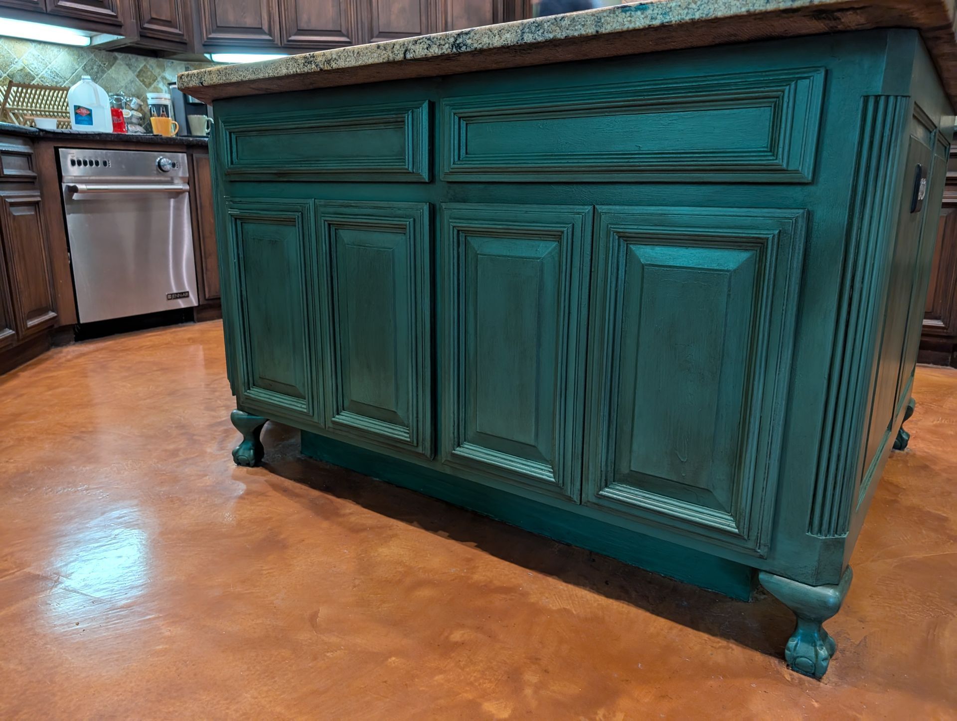 Kitchen island with teal cabinets and granite countertop. Stainless steel appliances in background.