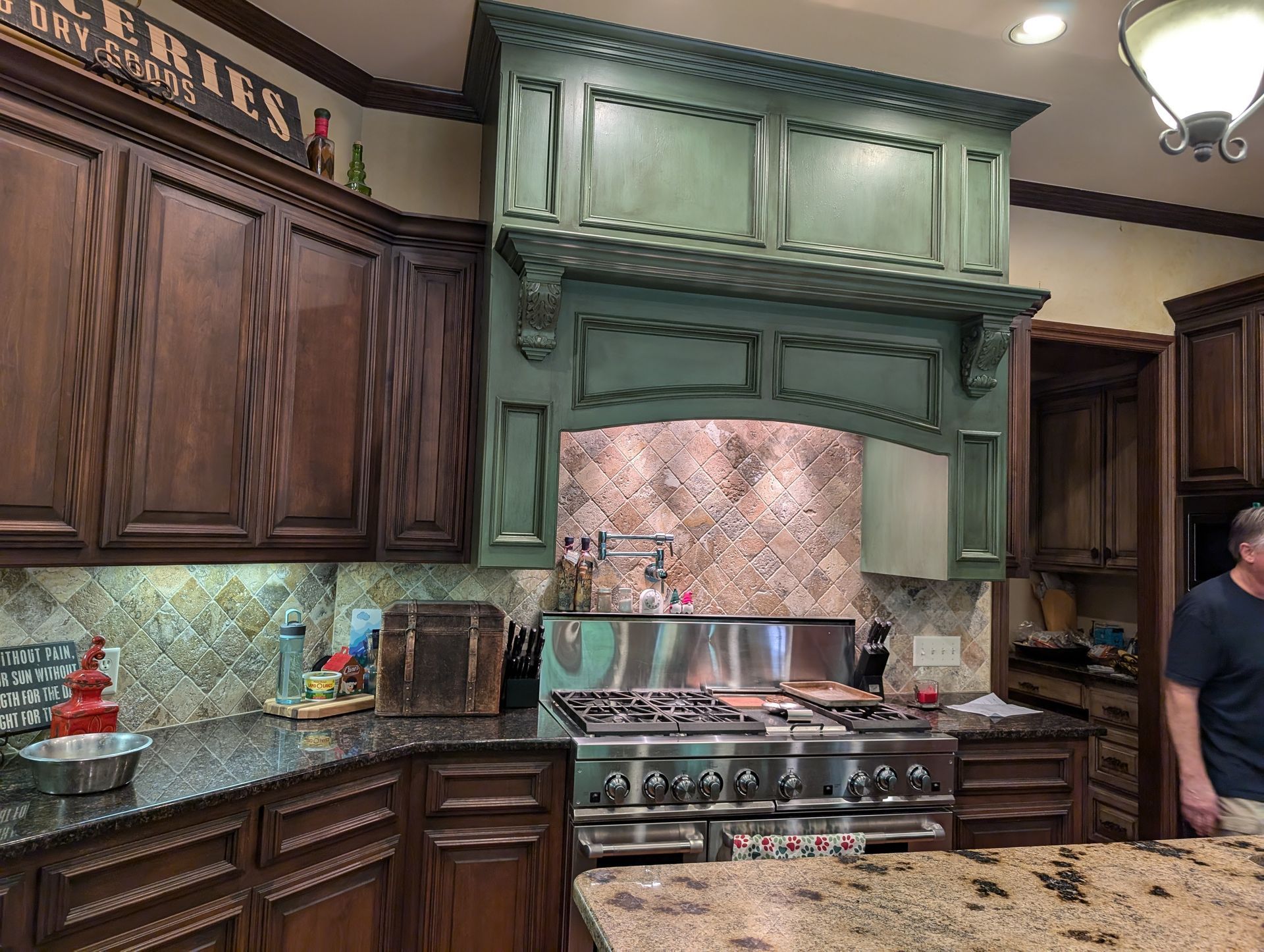 Kitchen with dark wood cabinets, green range hood, and stainless steel stove.