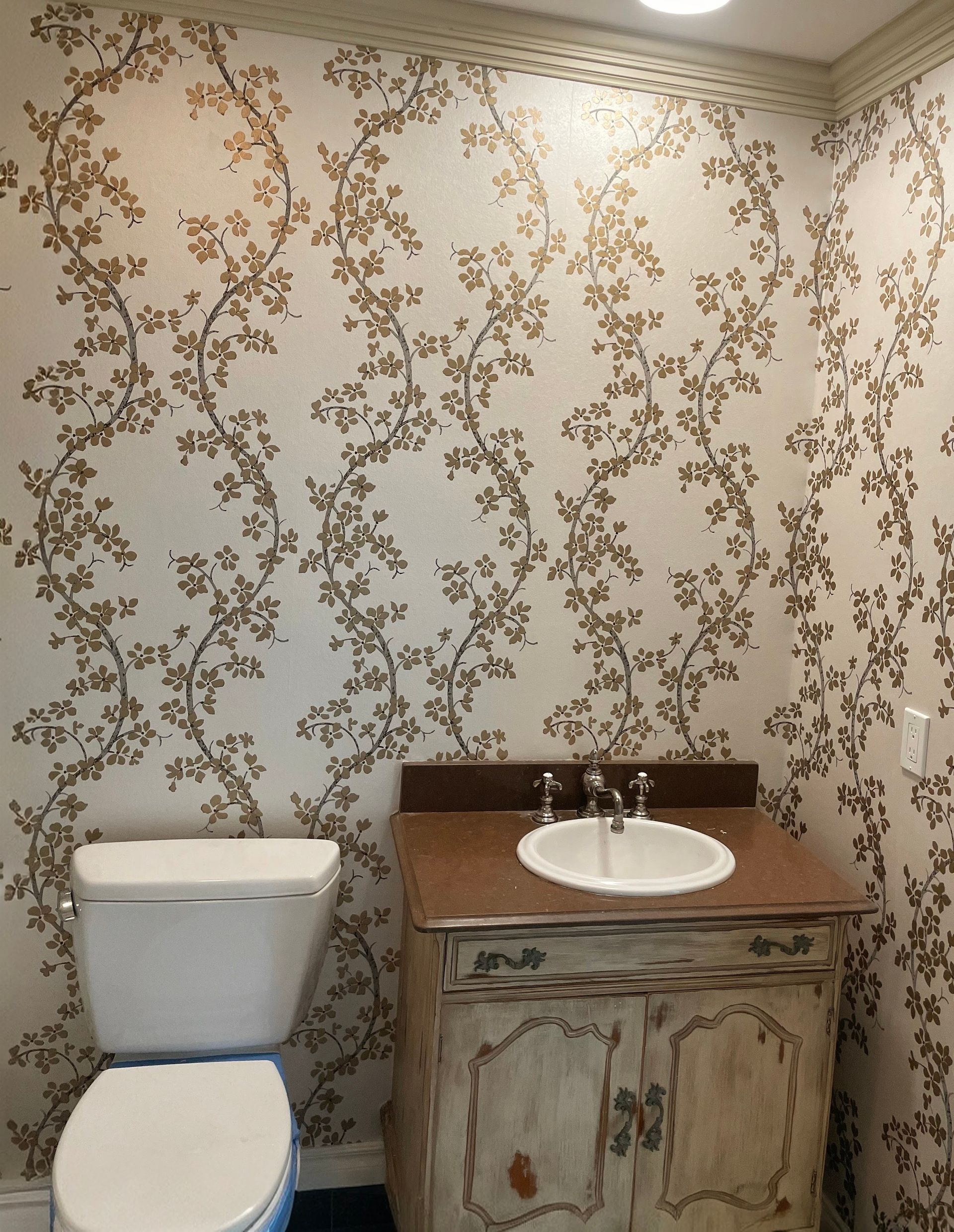 Powder room with floral wallpaper, toilet, sink, and aged wooden cabinet.