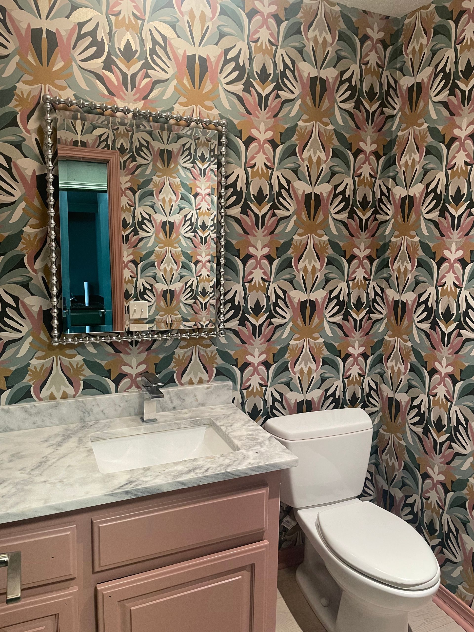 Powder room with floral wallpaper, pink vanity, marble countertop, and a toilet.