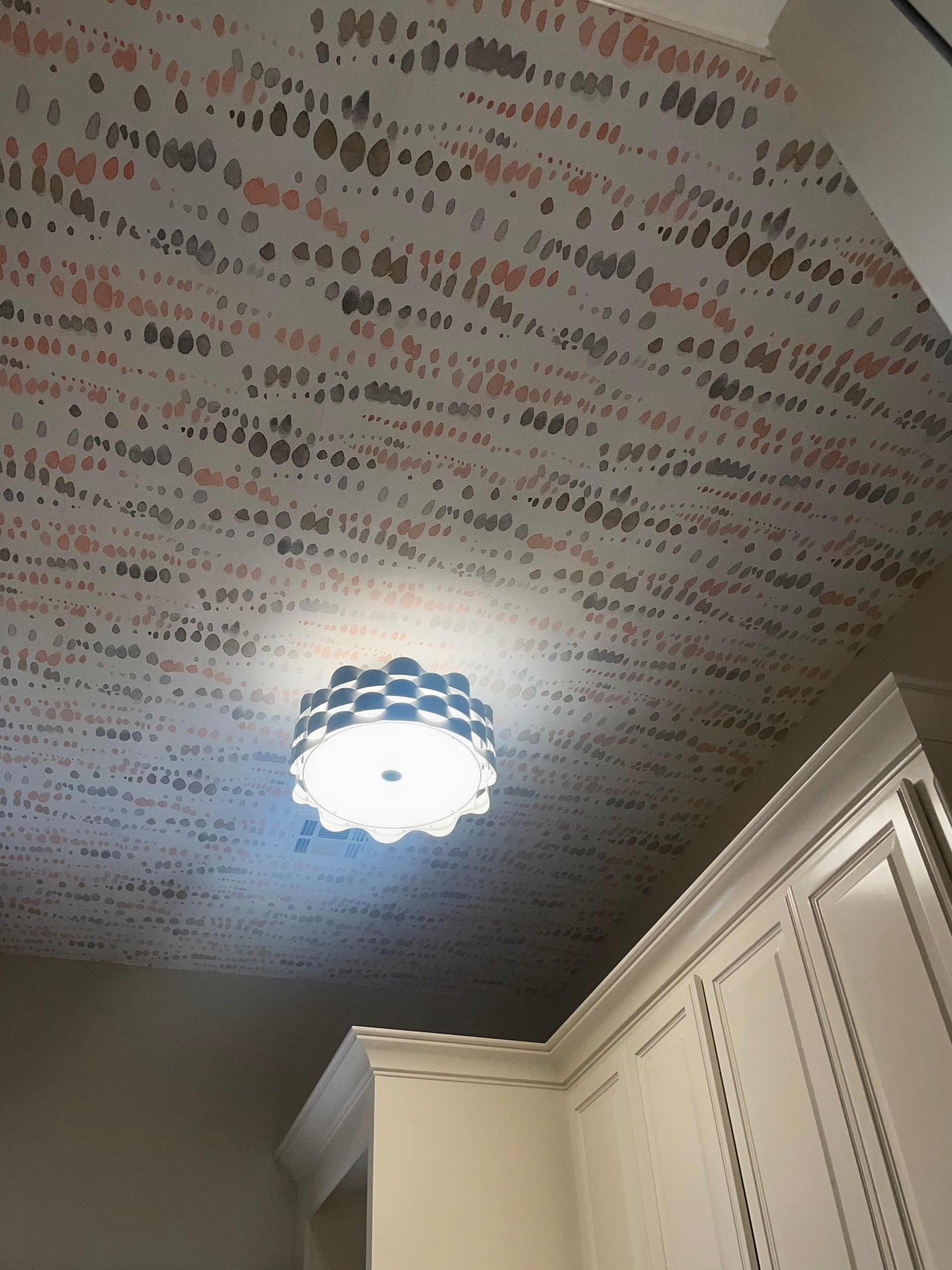 Ceiling with patterned wallpaper (gray, pink, brown) and a decorative light fixture over white cabinets.