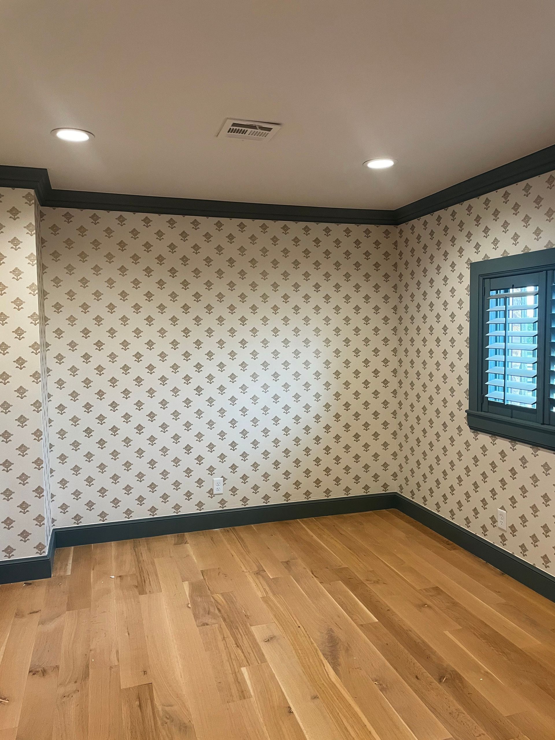 Empty room with floral wallpaper, wood floor, and blue trim.