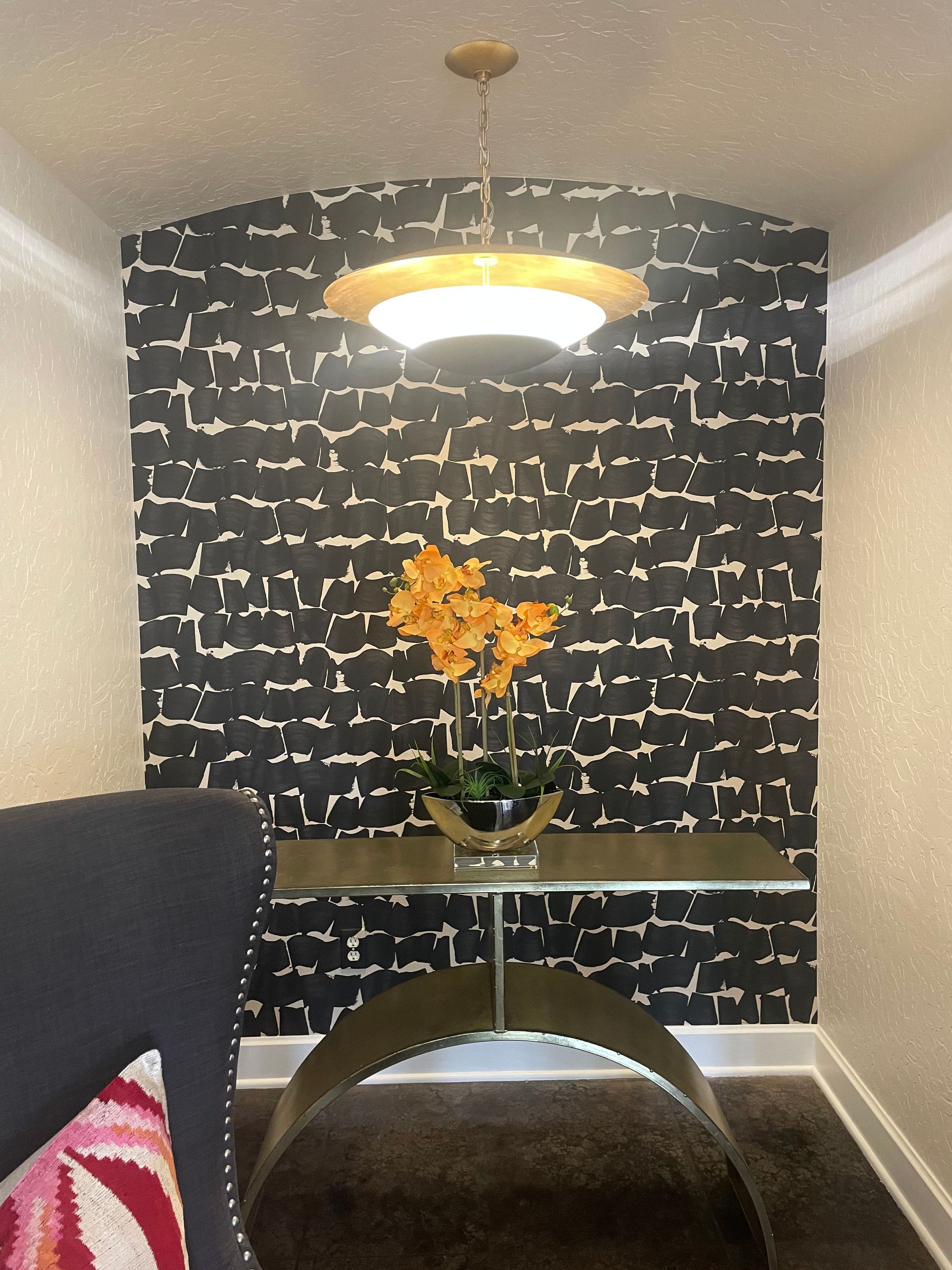 Black and white patterned wall with gold accents, console table, and orange flowers under a gold light fixture.