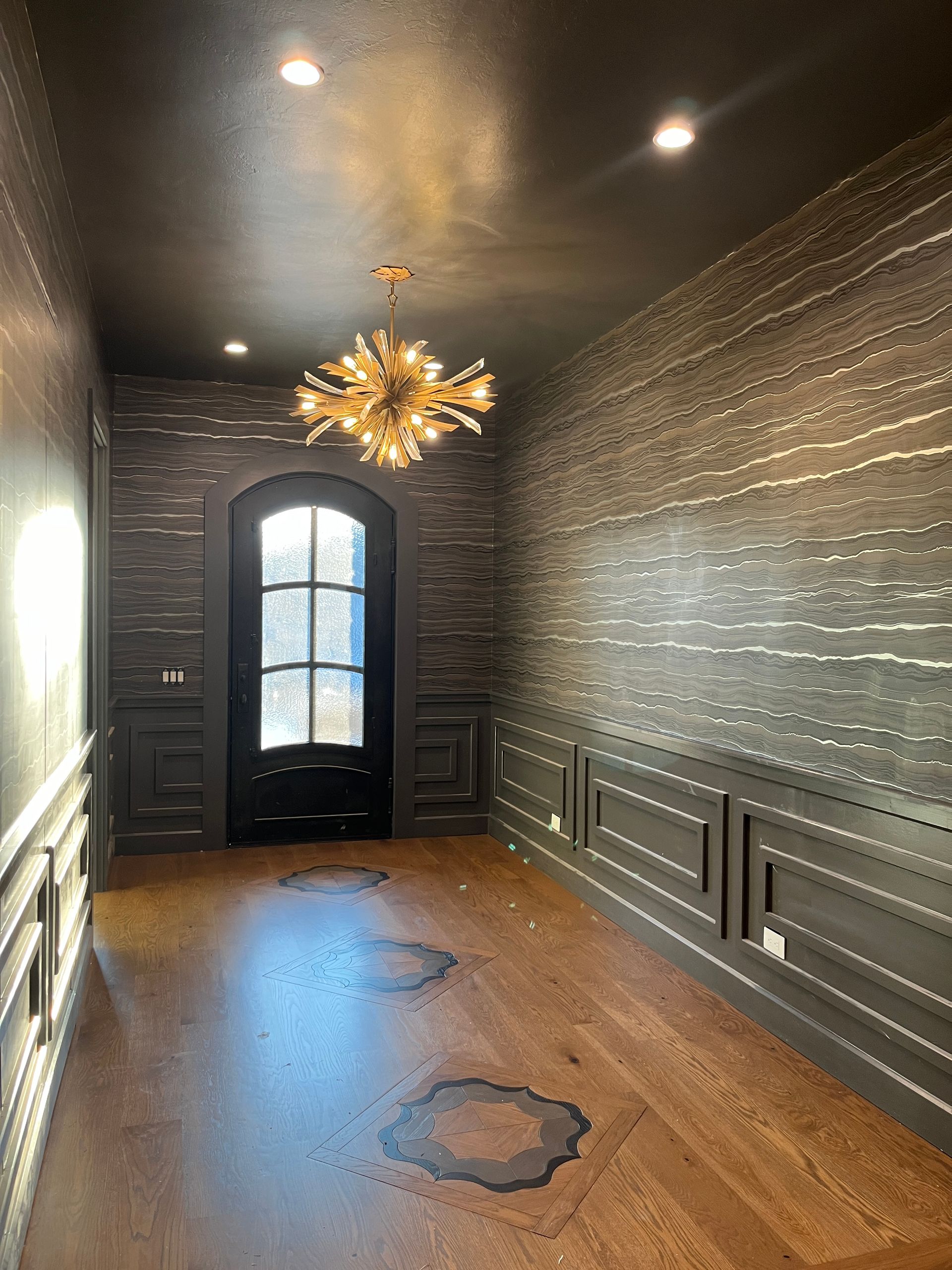 Dark room with wood floor, dark walls, arched doorway, and a golden chandelier.