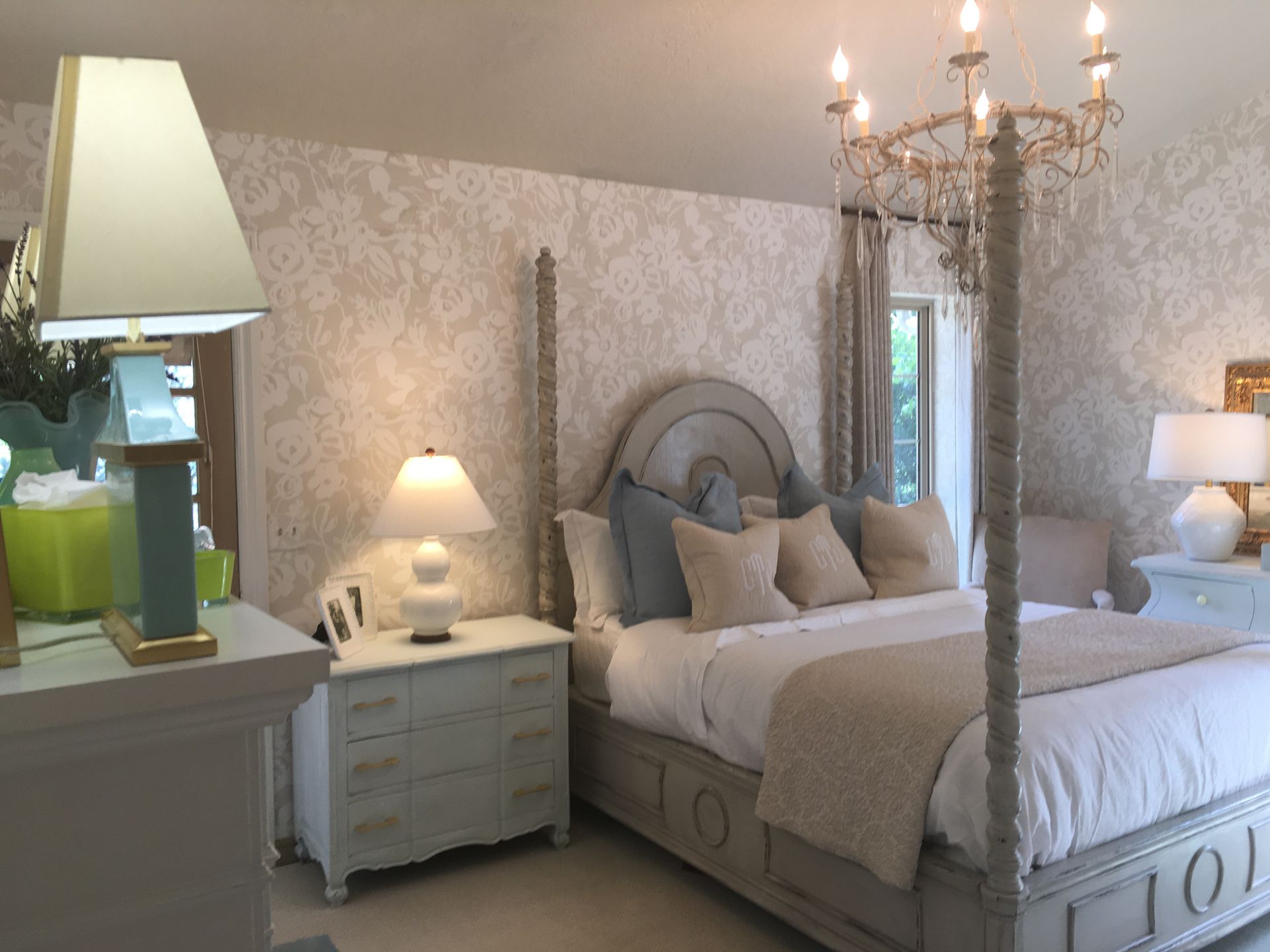 Bedroom with four-poster bed, wallpaper, light blue and cream furniture, and a chandelier.