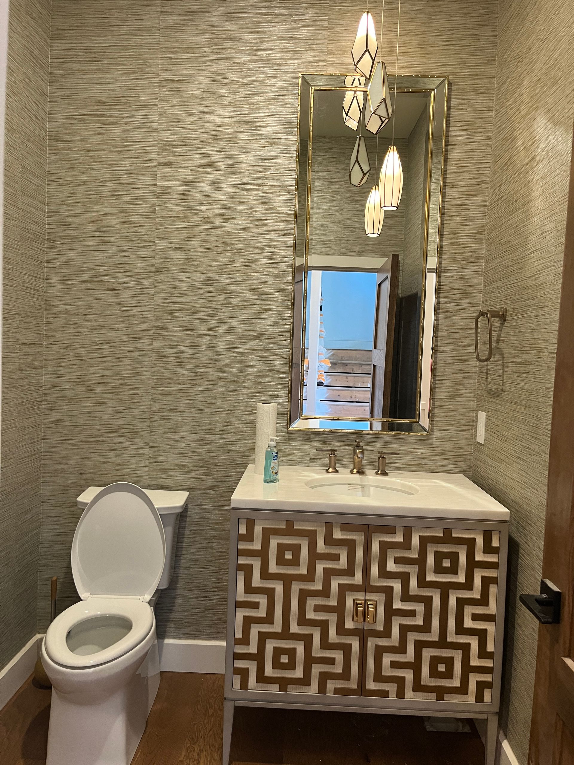 Small bathroom with patterned tile walls, a toilet, patterned vanity, and a mirror with chandelier lighting.