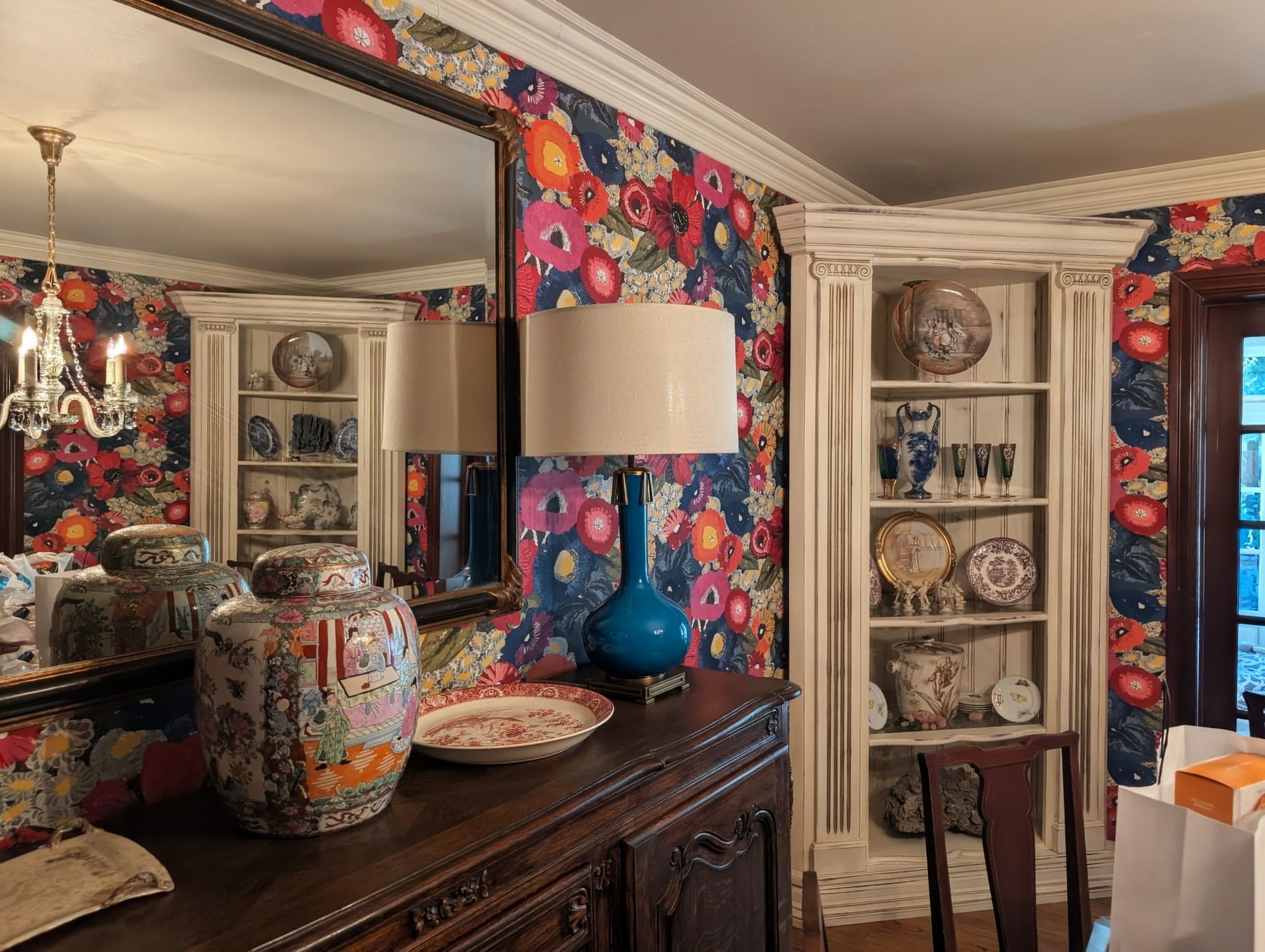Dining room with floral wallpaper, a buffet, mirror, and built-in shelves displaying china.