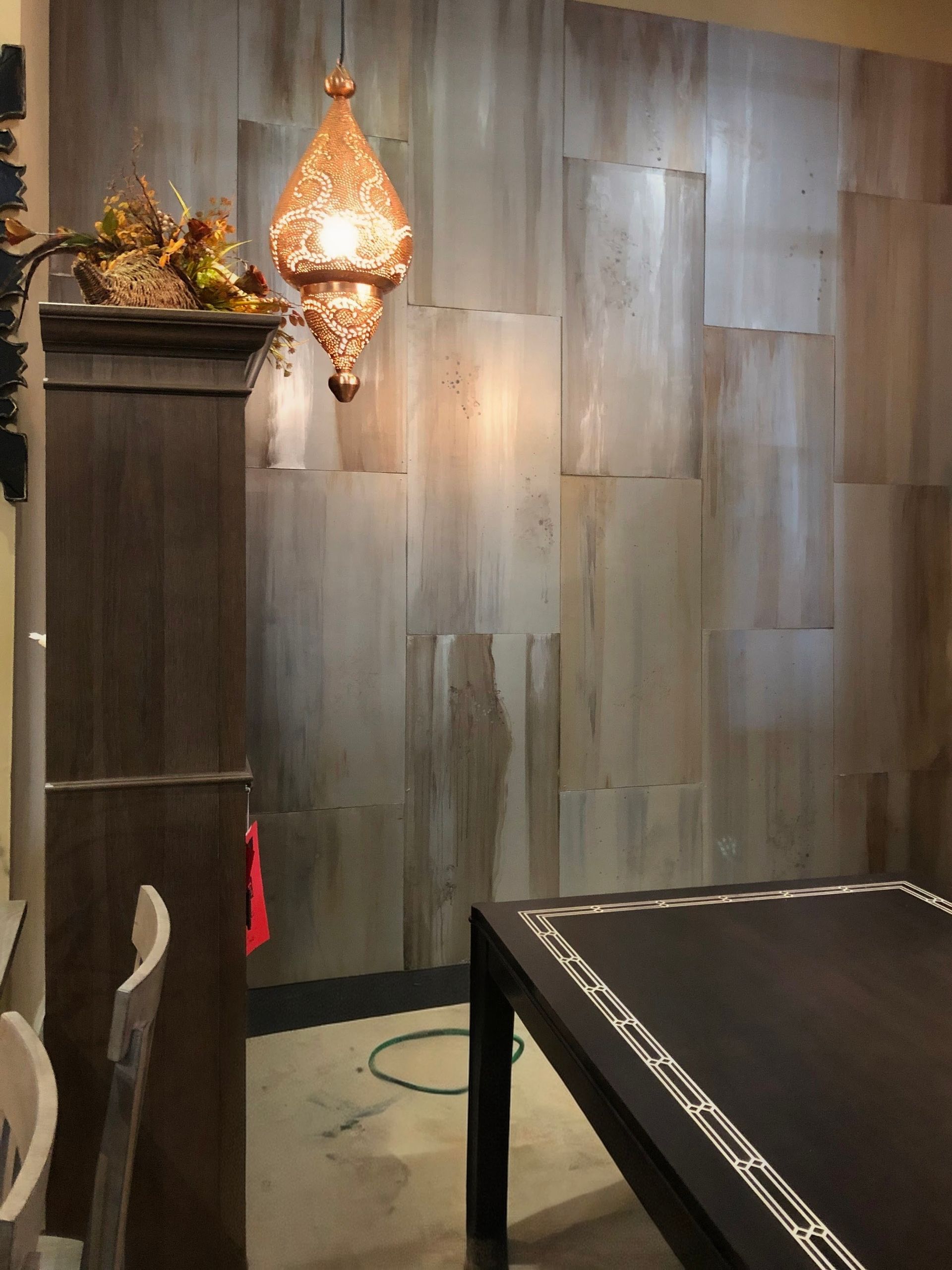 Dining room with wooden paneled accent wall, ornate pendant light, and dark table.