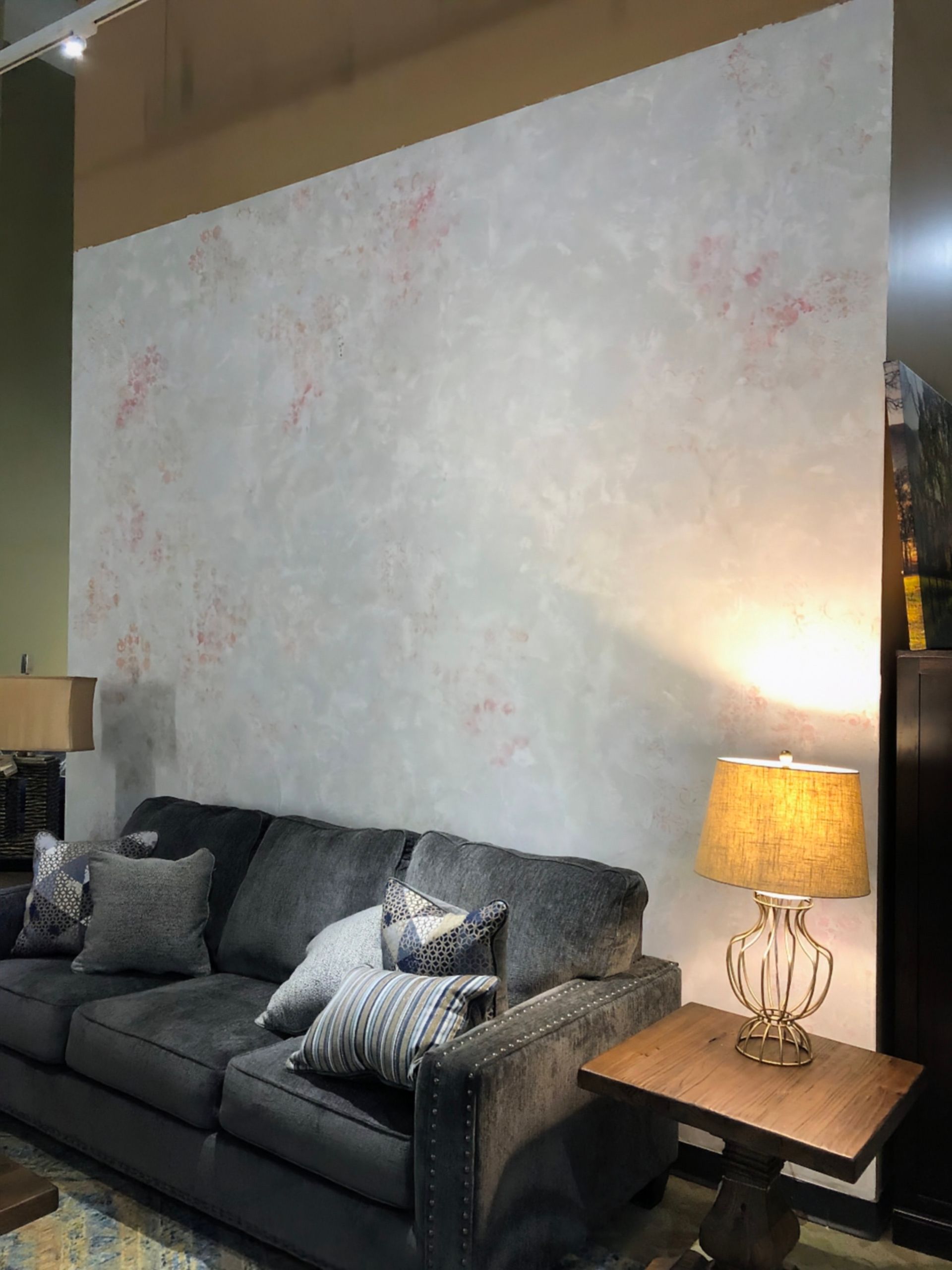 Gray sofa, lamp with a warm glow, and textured white wall with pink accents.