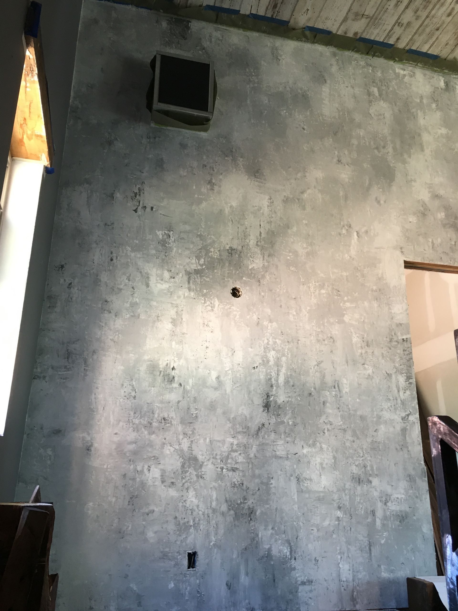 Gray textured wall with a vent, a hole, and an electrical outlet. Sunlight is coming in from the left.