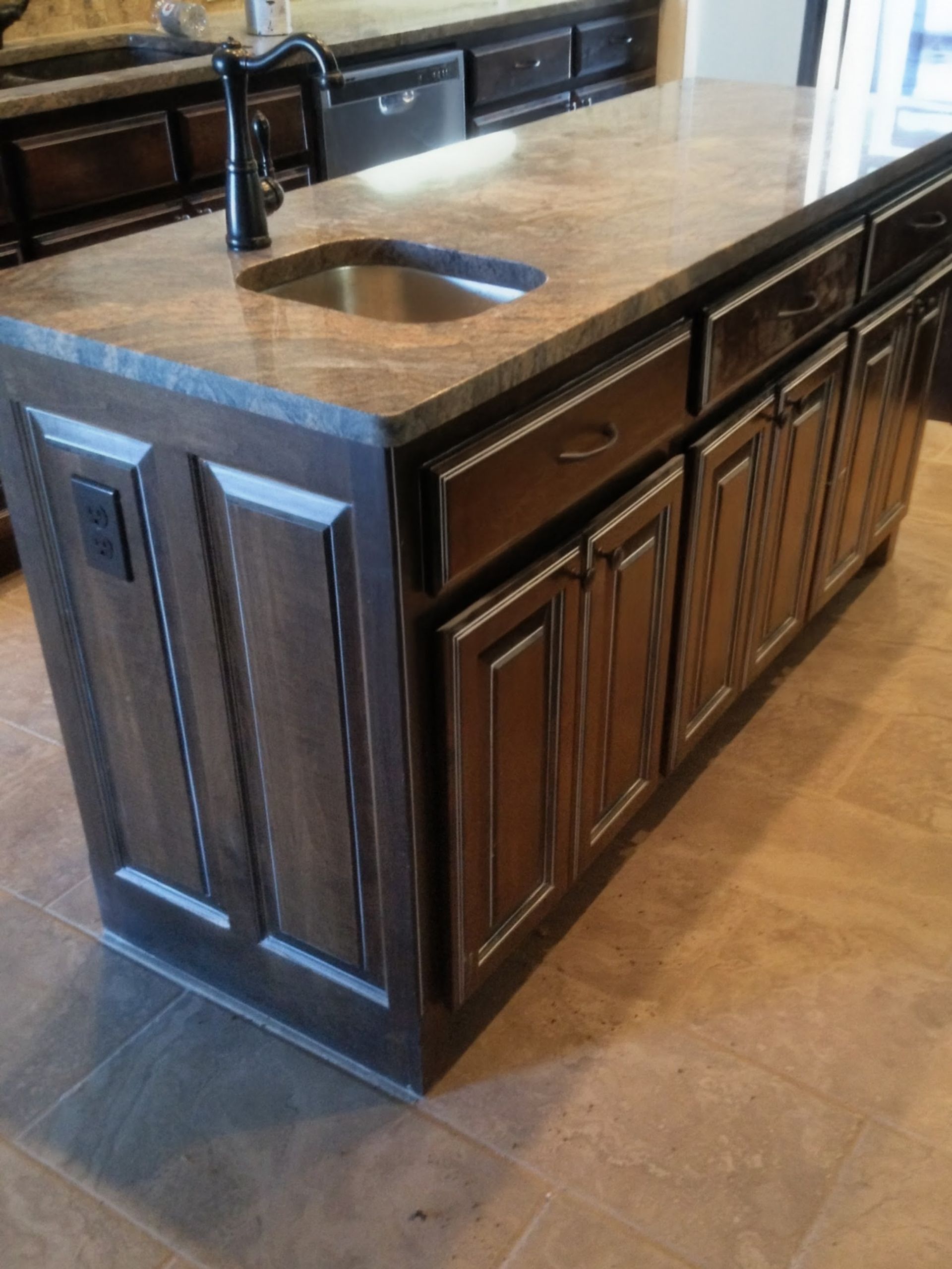 Kitchen island with dark wood cabinets, a granite countertop, and a stainless steel sink.