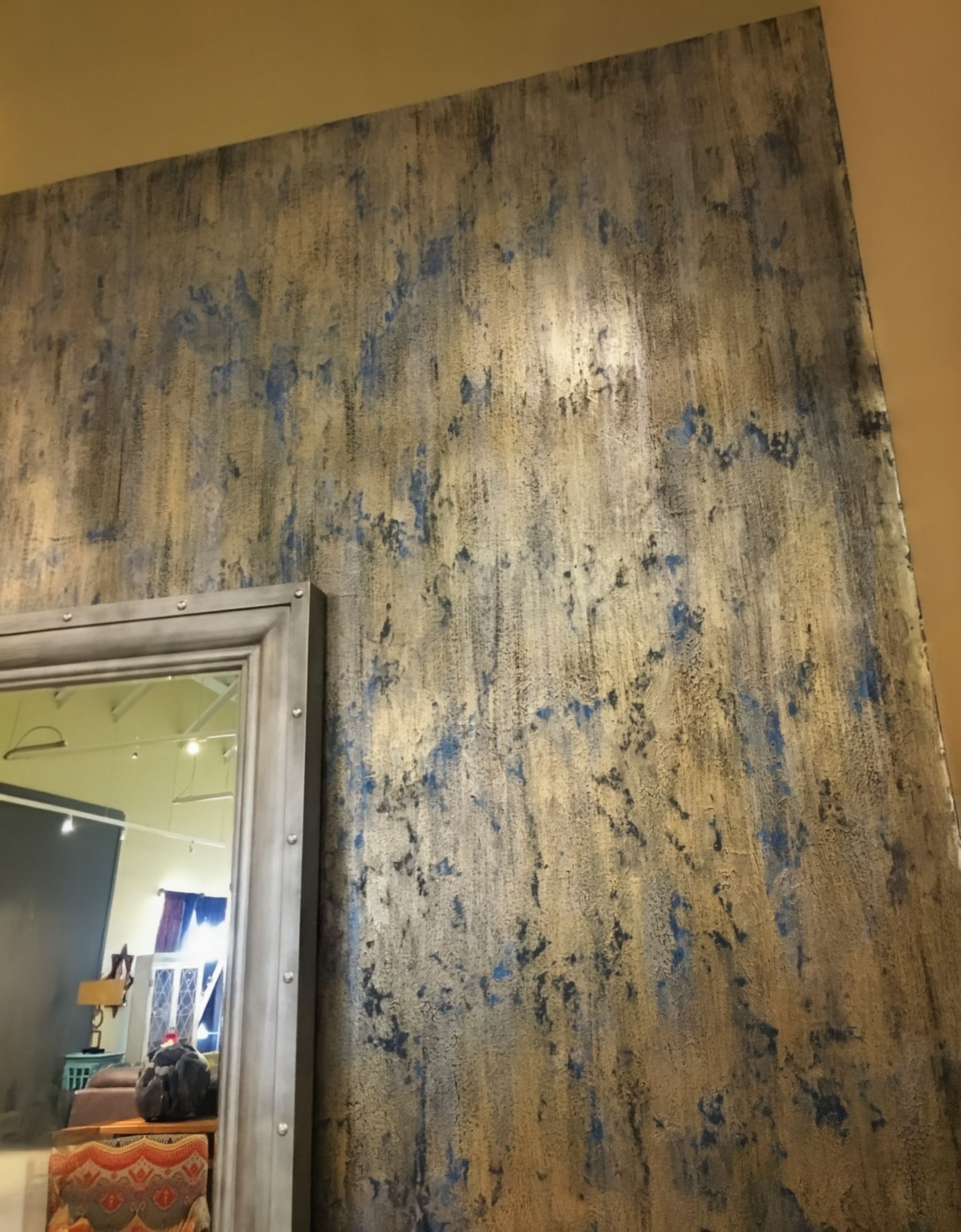 Textured wall with vertical streaks of blue and gold paint, next to a mirror.