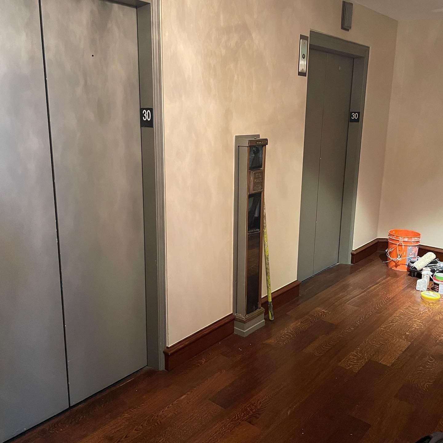 Two elevator doors labeled 30 and 31 in a hallway with wood flooring and construction materials.