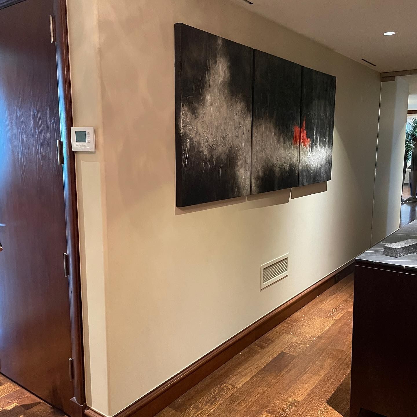 Hallway with abstract art, dark wood door, light walls, and hardwood floor.
