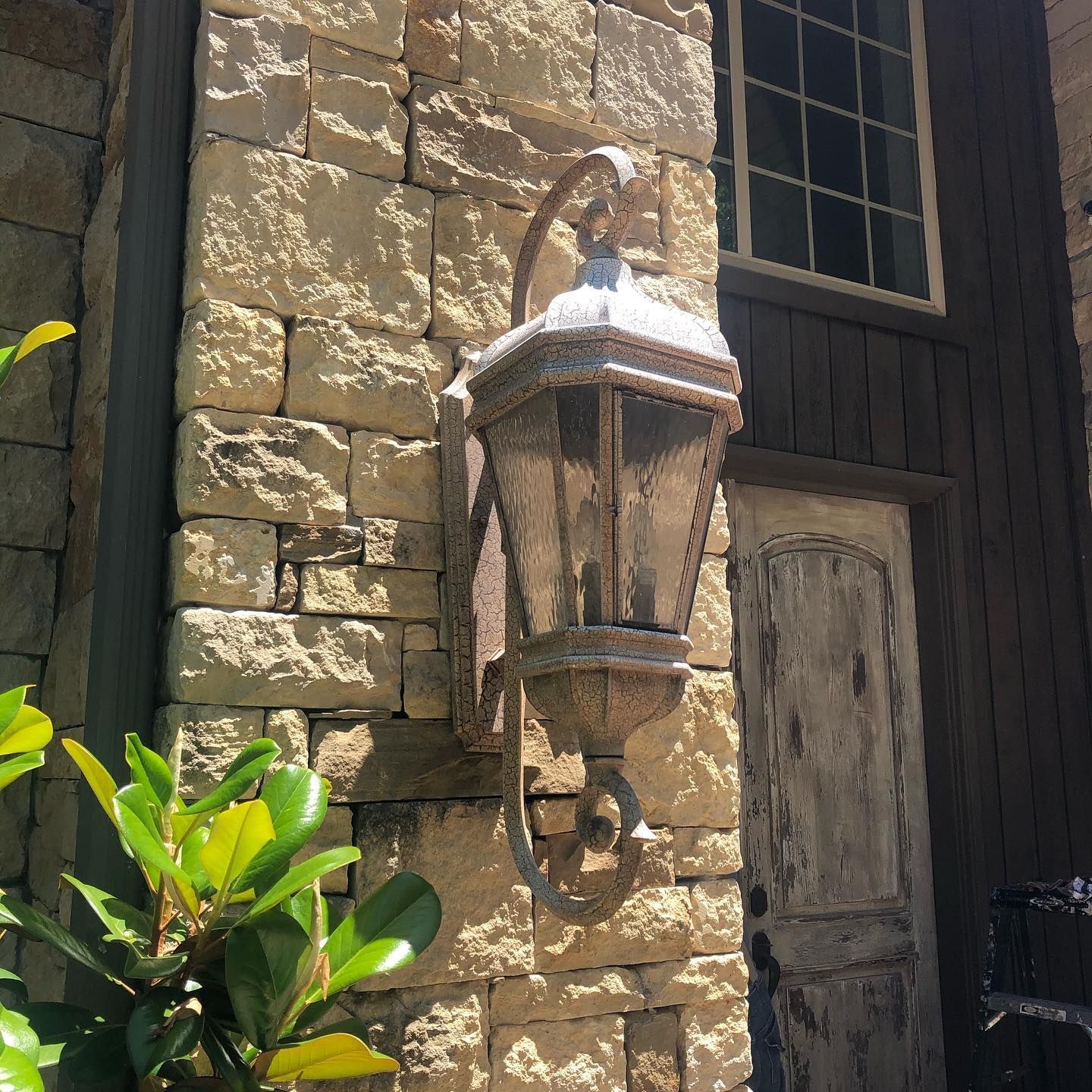 Large, ornate lantern on a stone wall next to a weathered wooden door and window.