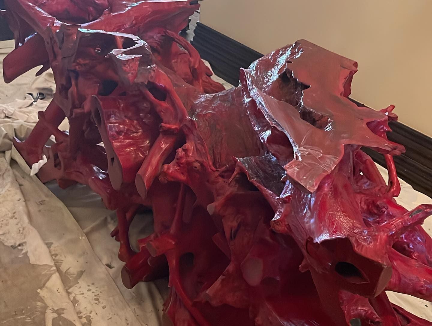 Red painted, intricate wooden sculpture on a white cloth, next to a brown wall.
