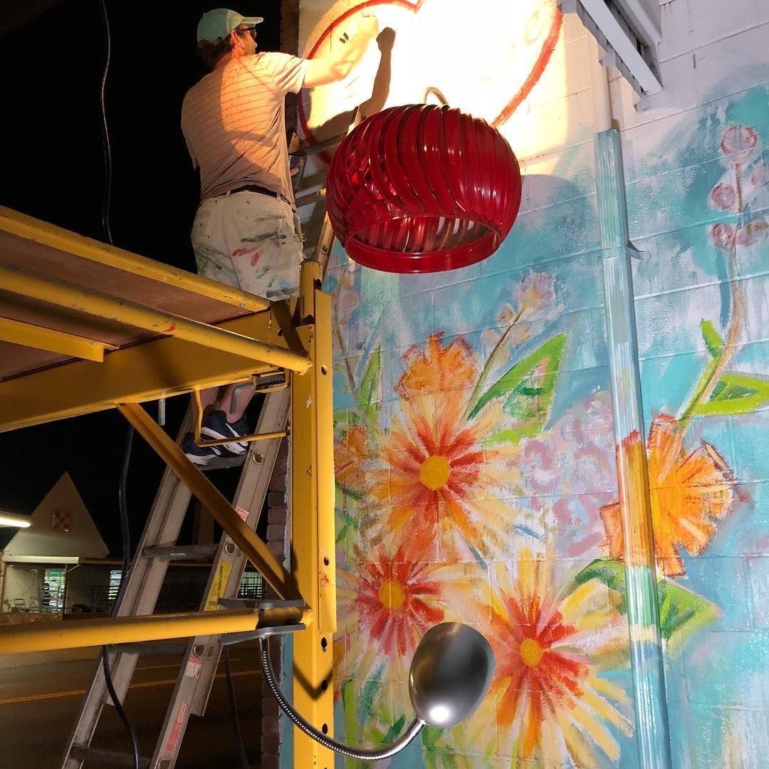 Person on a scaffold installing a red lantern to a mural of flowers.