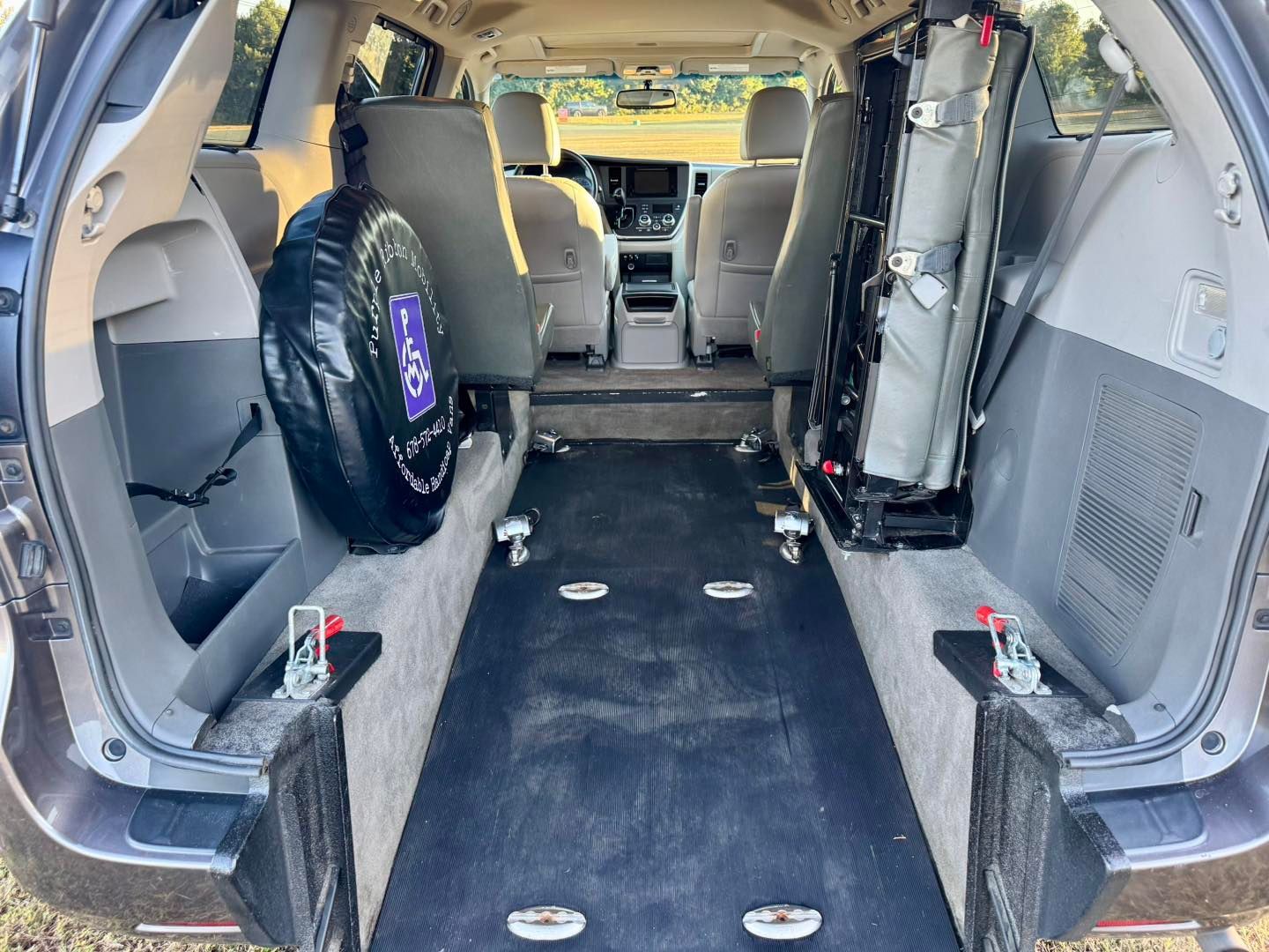 Inside of a modified accessible van with ramp and wheelchair tie-downs. Spare tire and seats are visible.
