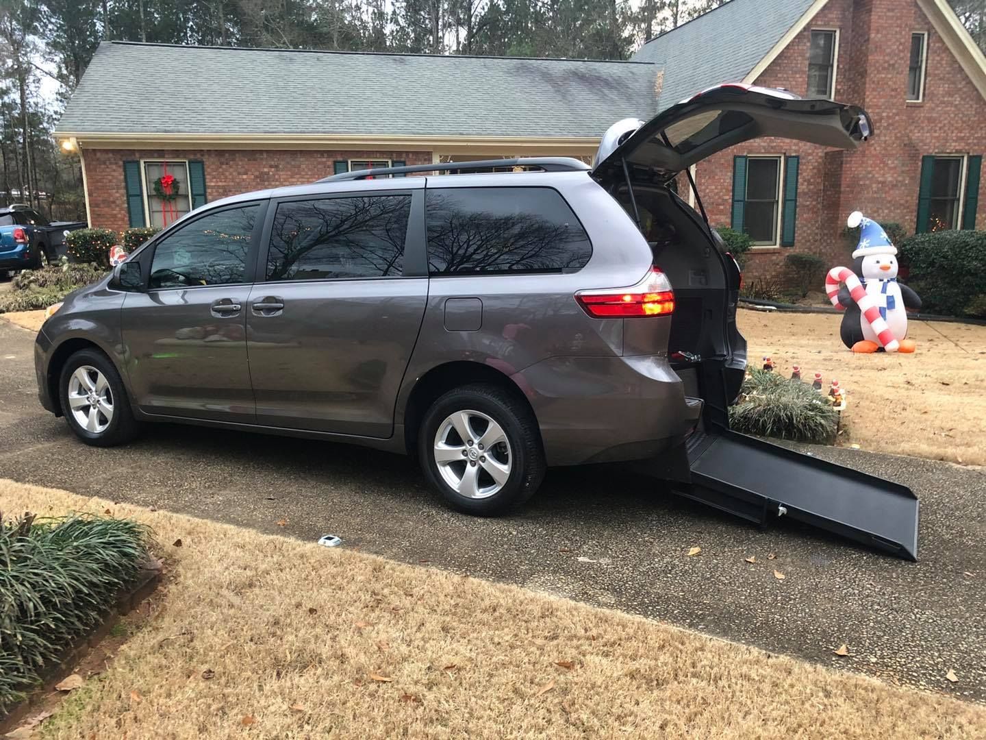 Gray minivan with open ramp parked in front of a house, possibly for accessibility.