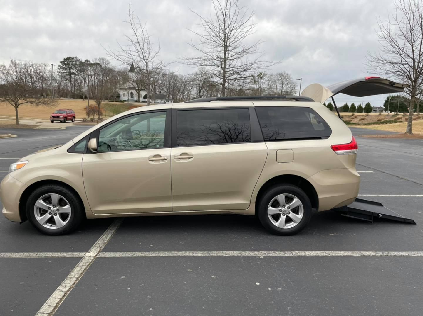Gold minivan with a ramp extending from the rear, parked outdoors.