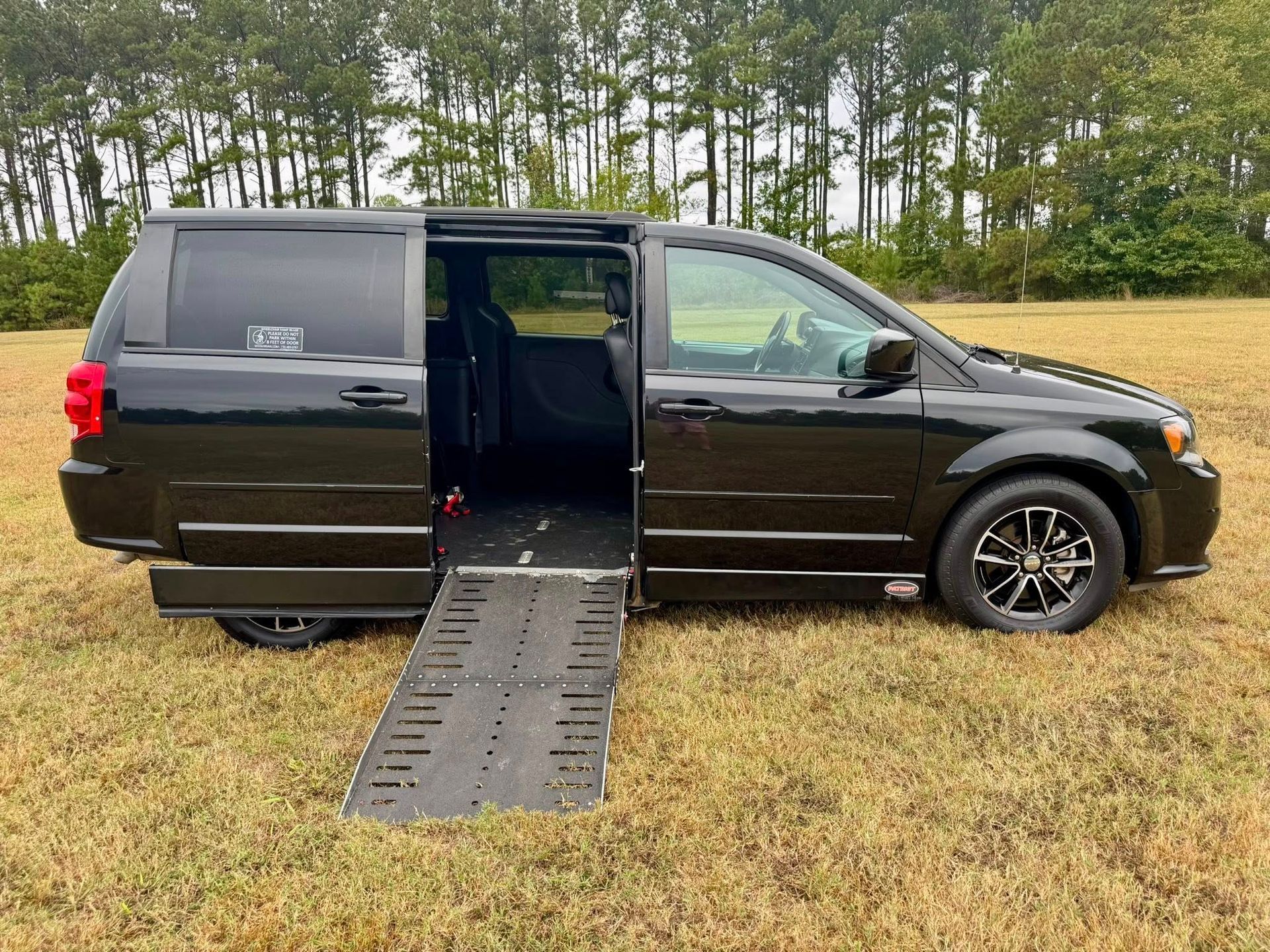 Black wheelchair accessible van with ramp extended on grassy field.