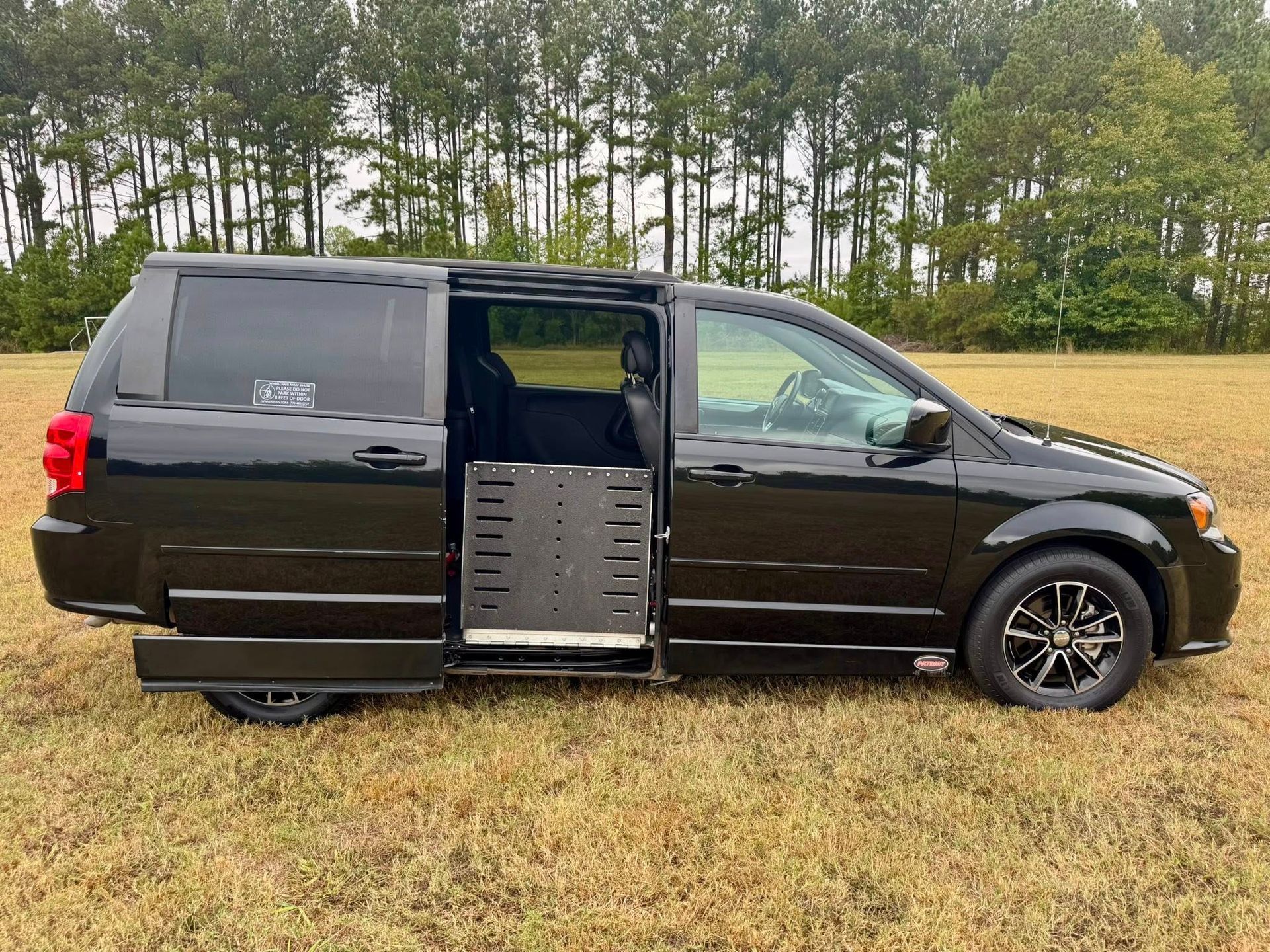 Black wheelchair-accessible van with a ramp extended, parked on grass field, overcast day.