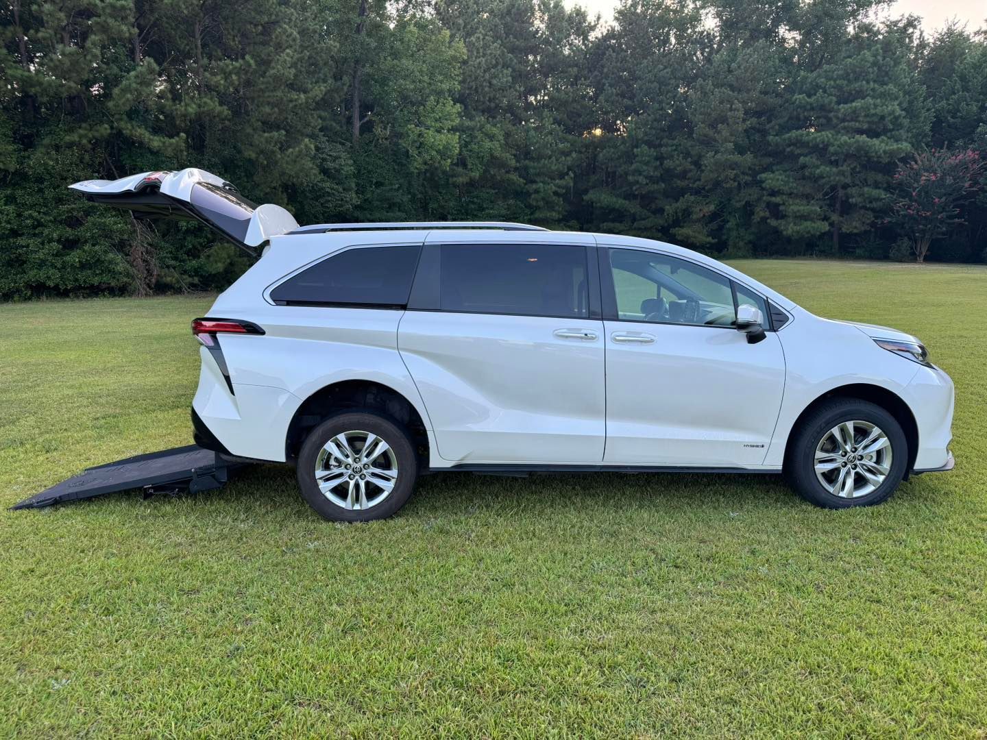 White accessible minivan with ramp deployed on green grass. Back door open.