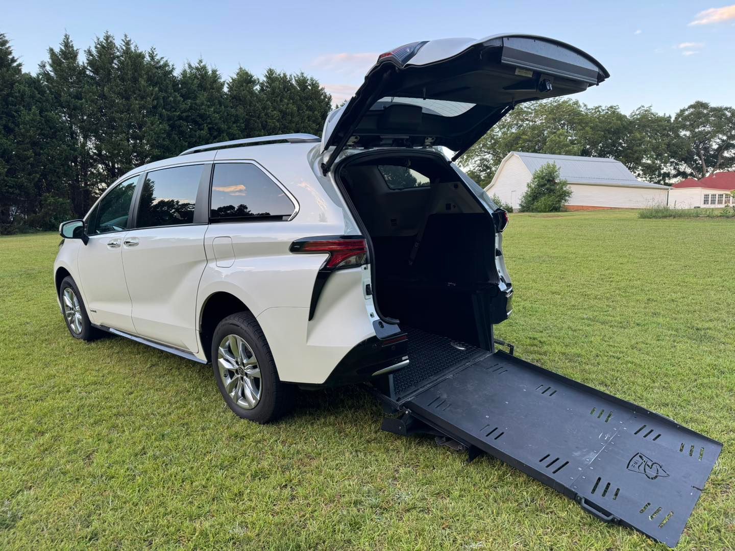 White minivan with ramp extended, parked on grass.