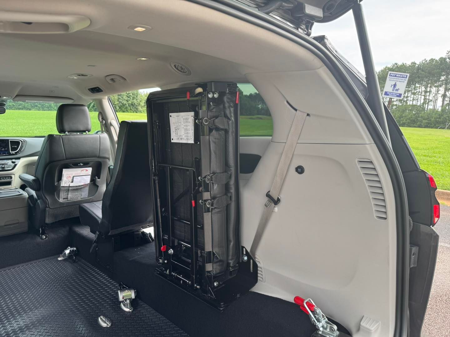 Interior of a van with a folded wheelchair accessible seat. The seat is black, metal frame.