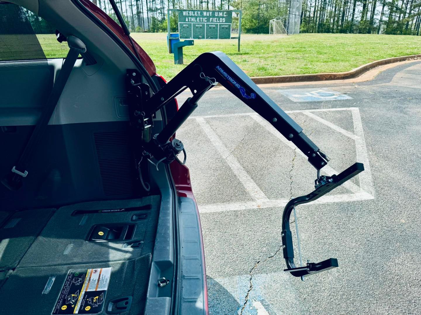 Wheelchair lift extended from a red van's open trunk in a parking lot.