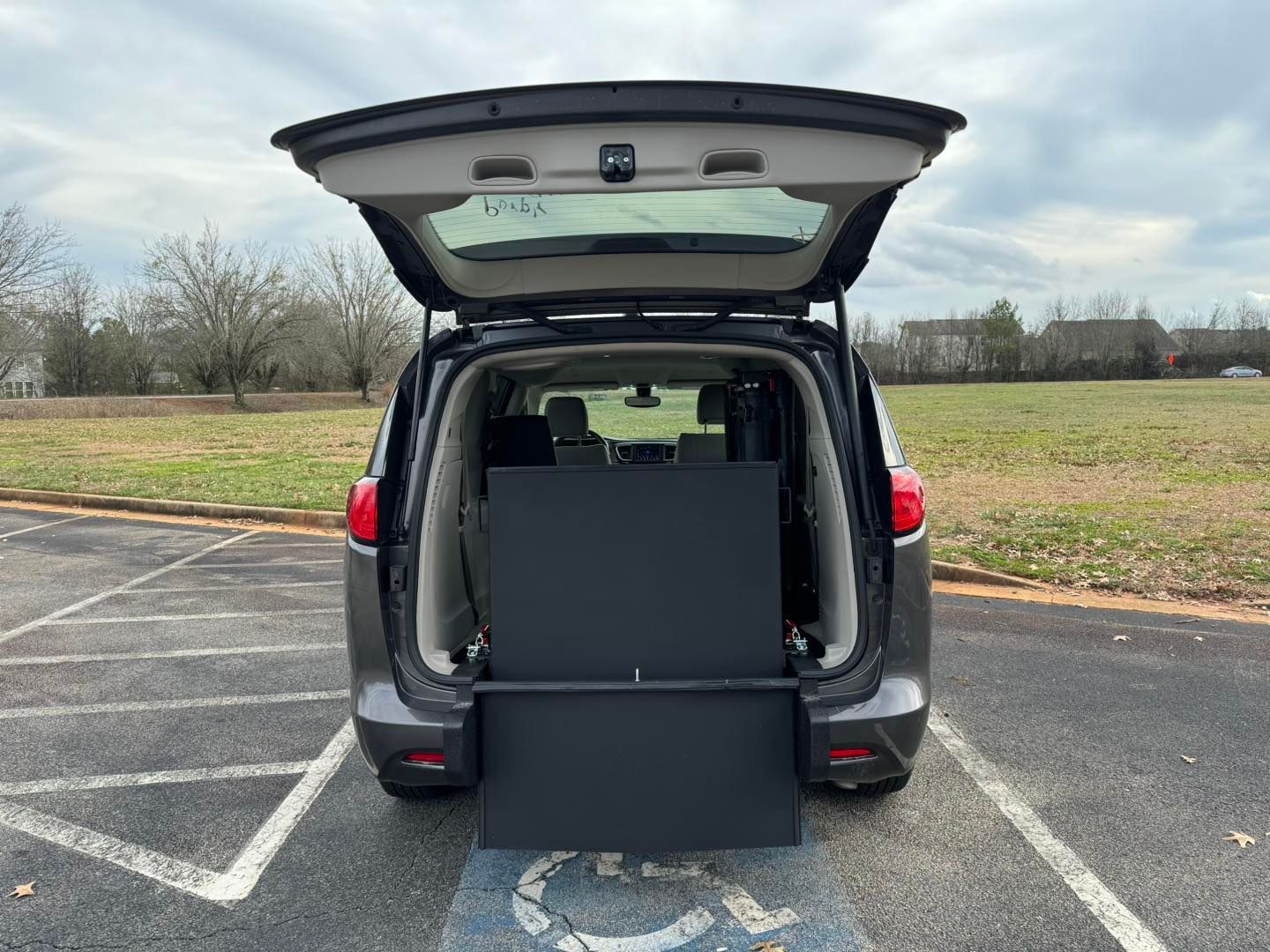 Dark gray minivan with open liftgate and deployed wheelchair ramp, parked in a handicapped parking space.
