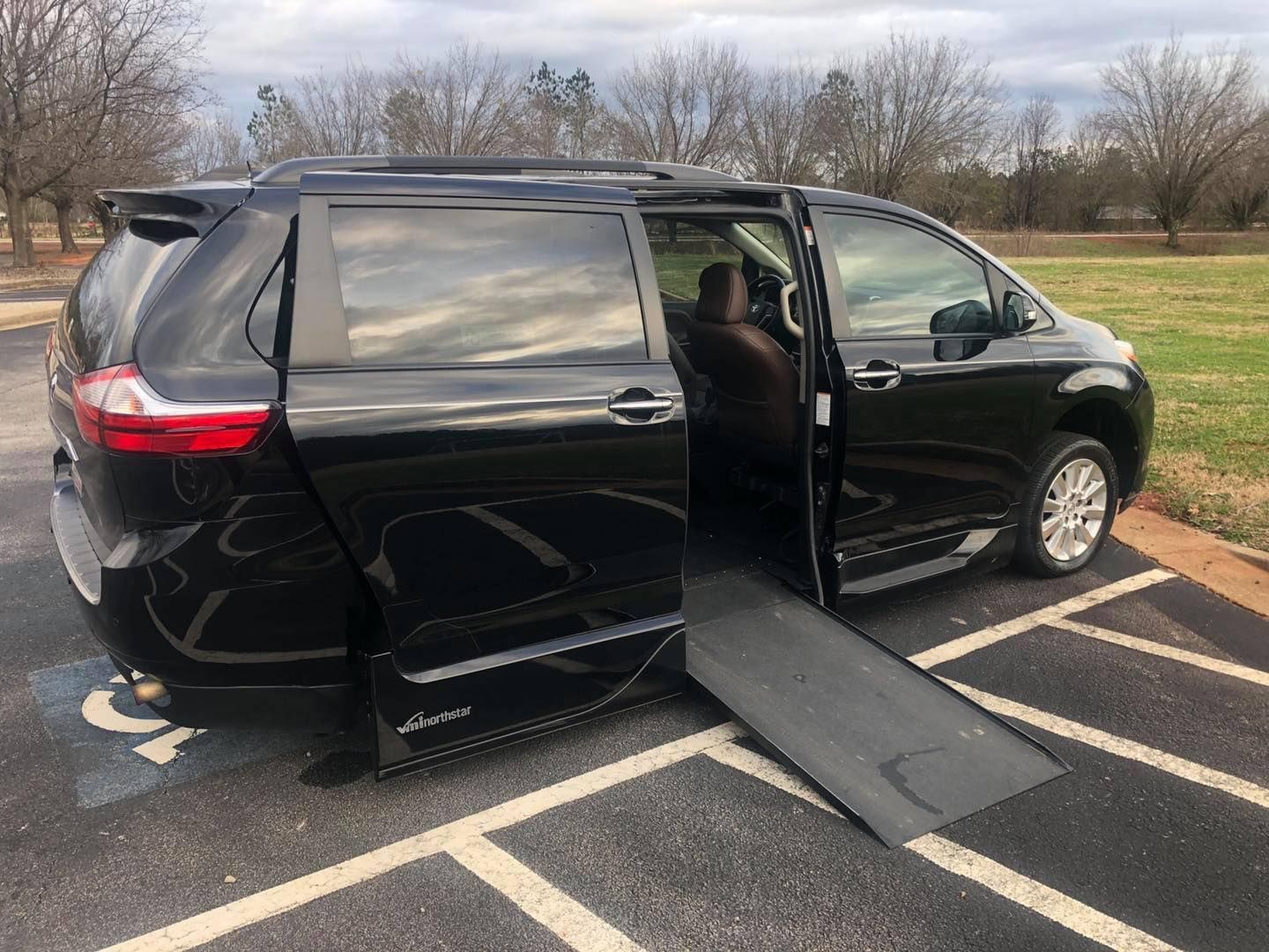 Black wheelchair-accessible van with ramp extended, parked in a marked spot.