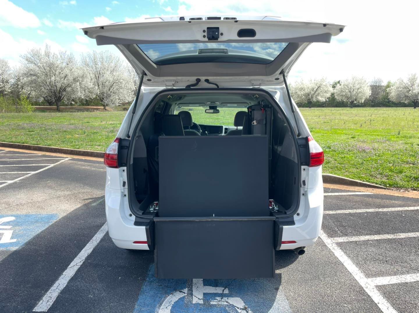 White van with open lift gate and ramp, parked in a handicapped spot.