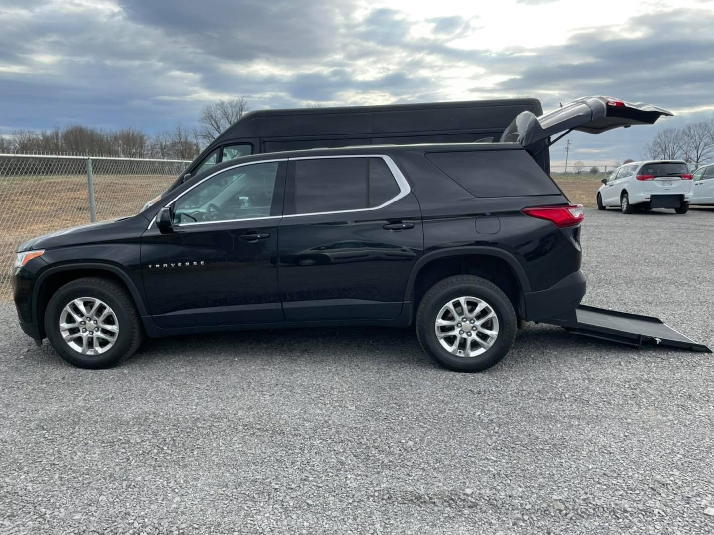 Black SUV with a ramp extended from the rear, parked on gravel.