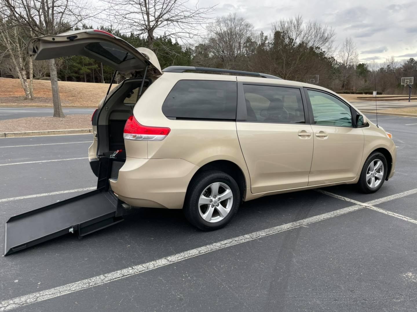 Tan minivan with wheelchair ramp deployed on asphalt parking lot.