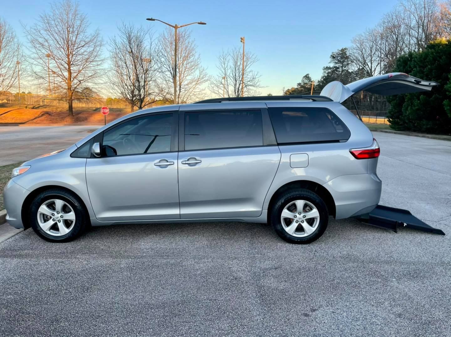 Silver minivan with a wheelchair ramp extended on paved surface.