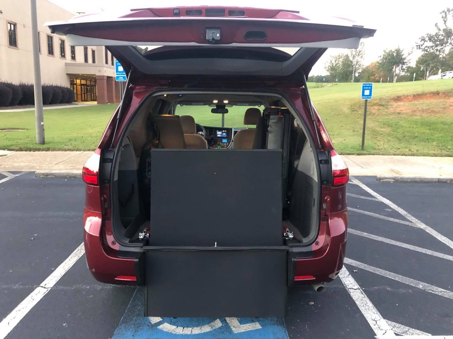 Red minivan with opened rear, showing a wheelchair ramp. Parked in a handicapped parking spot.