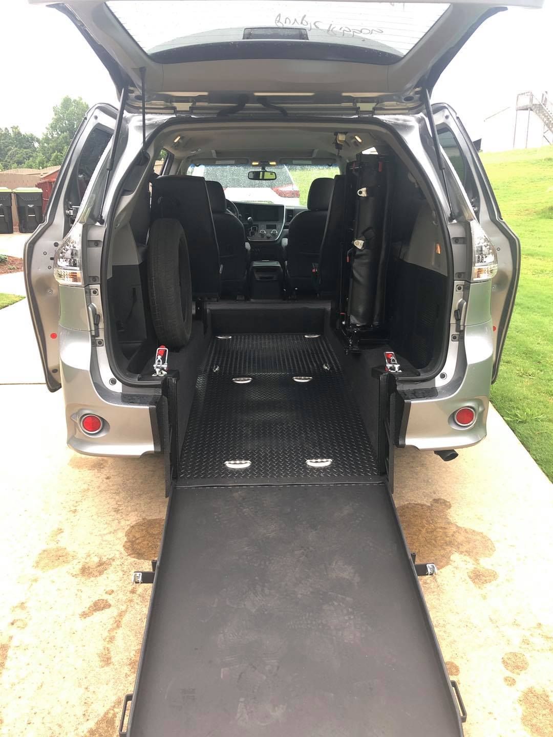 Rear view of a silver minivan with a wheelchair ramp extended.