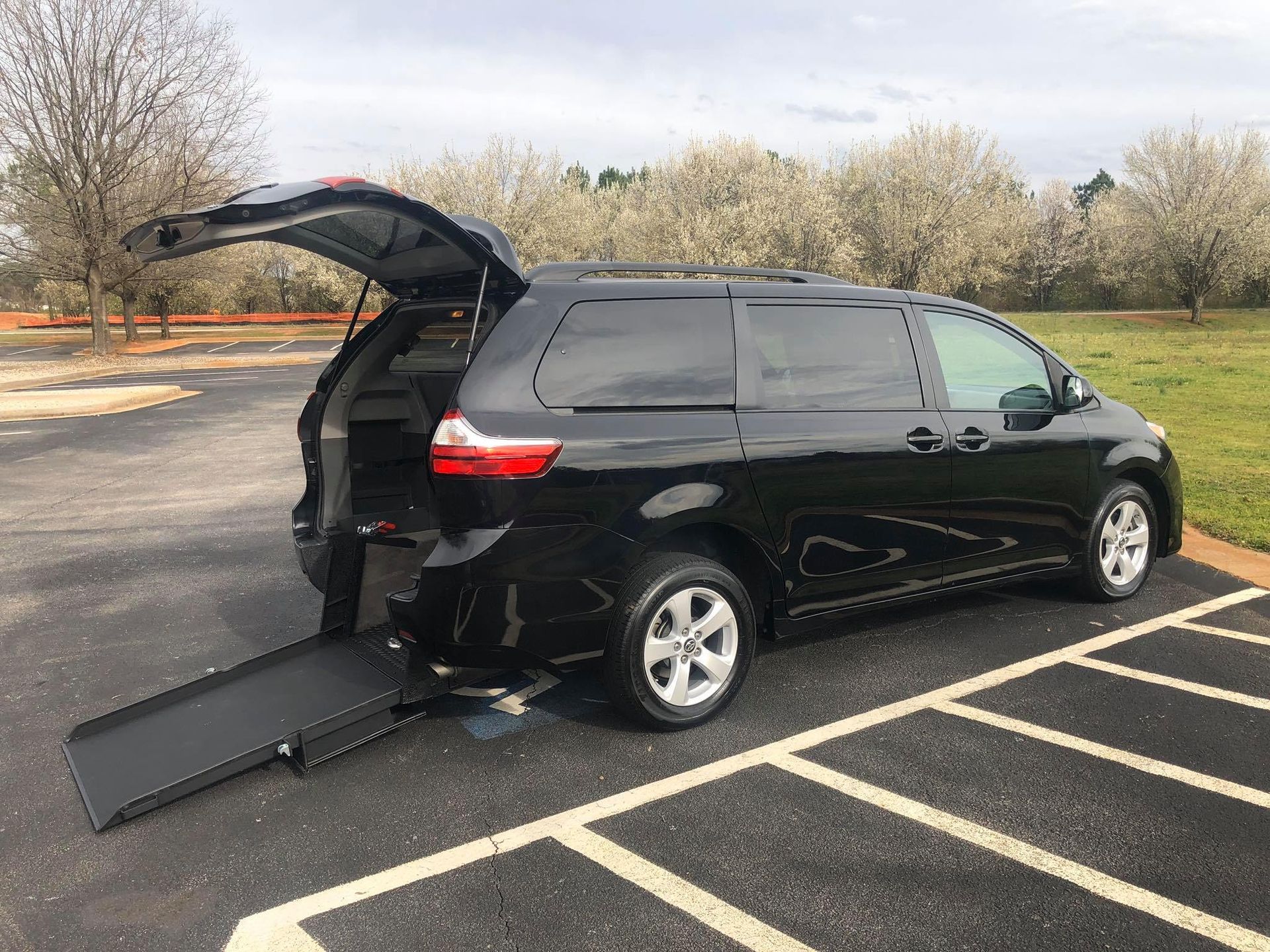Black minivan with a ramp extended, parked on asphalt, lift gate open.