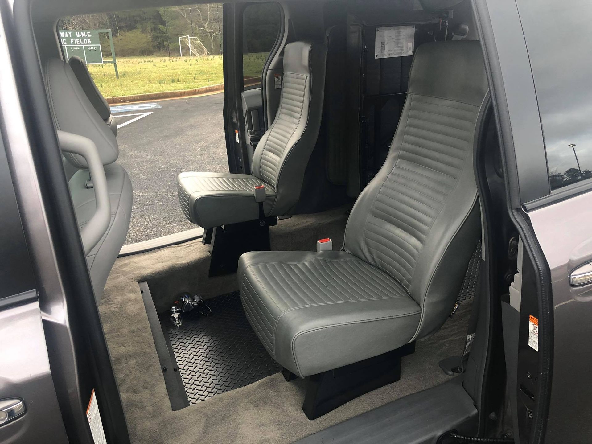 Interior of a modified van with two gray, high-backed seats, open door, and accessible floor.