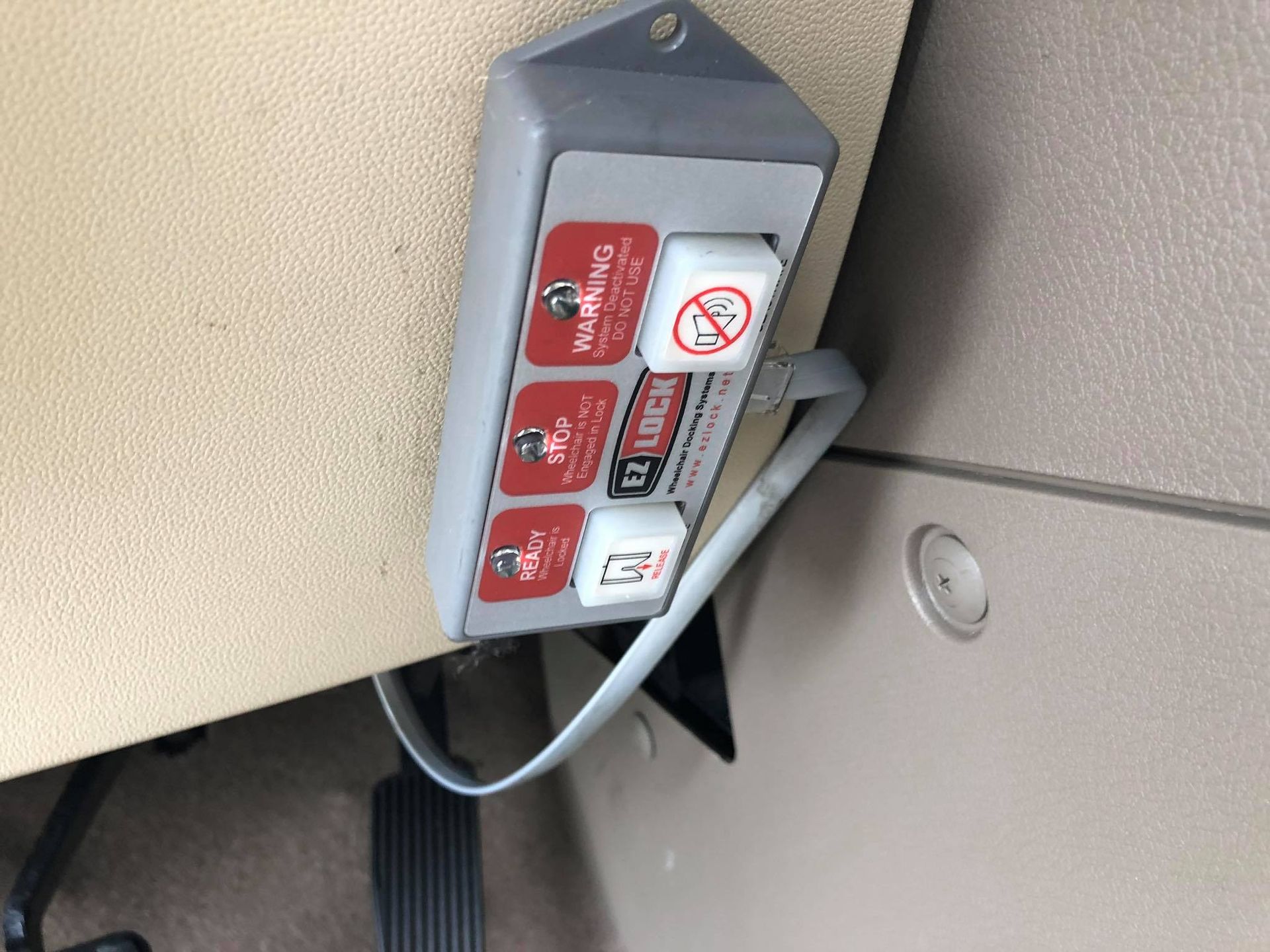 Gray control box with red and white buttons attached to a beige panel. Warning symbols and text.