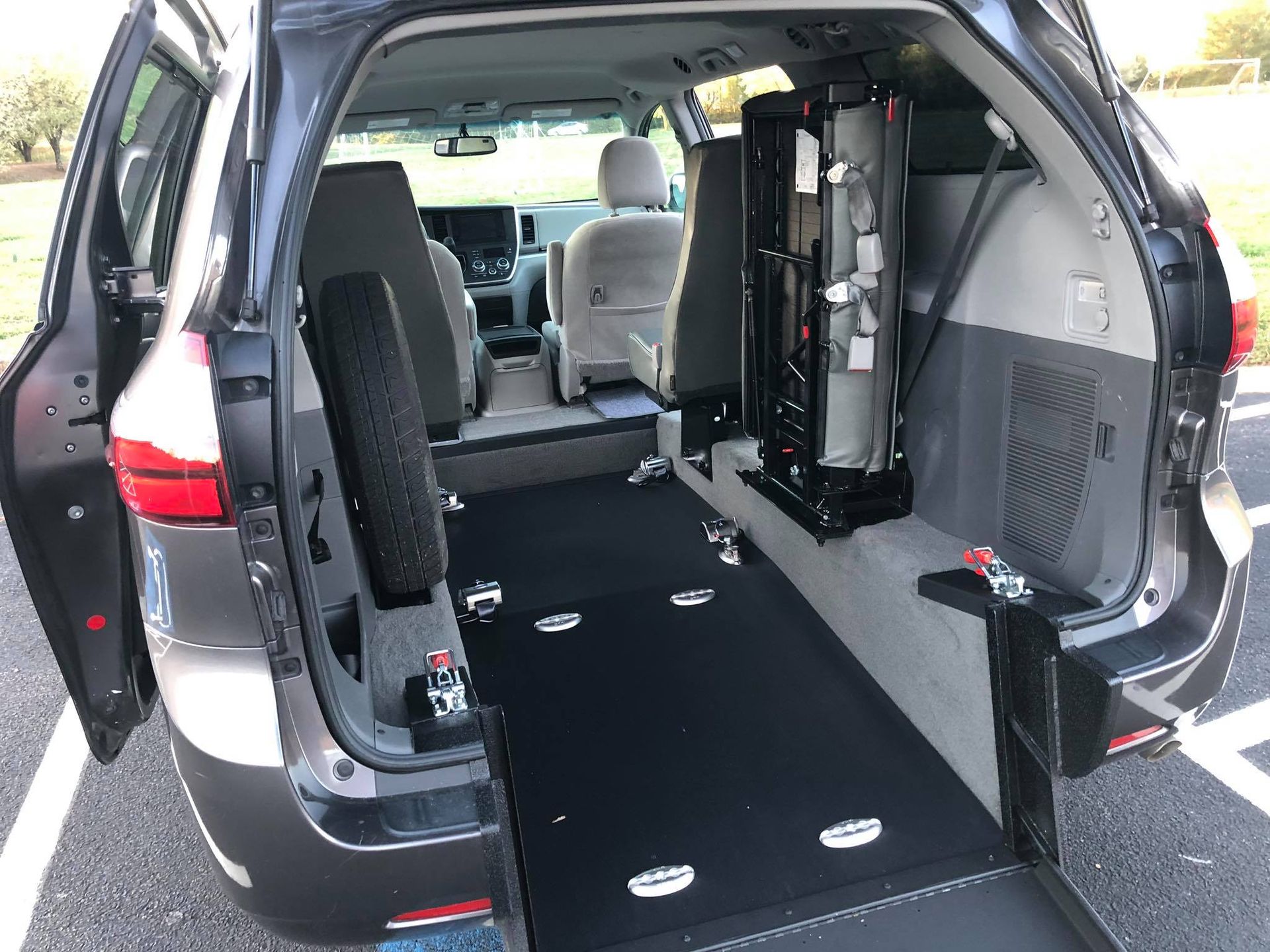 Inside of a wheelchair-accessible minivan with a ramp and lift. Black interior with open doors on an outdoor parking lot.