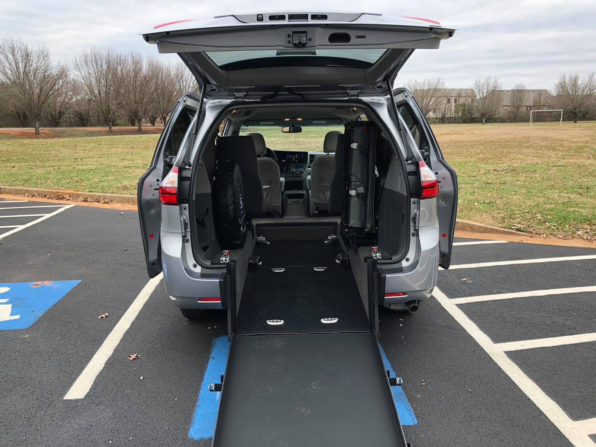 Gray minivan with rear ramp extended in a parking space designated for accessibility.