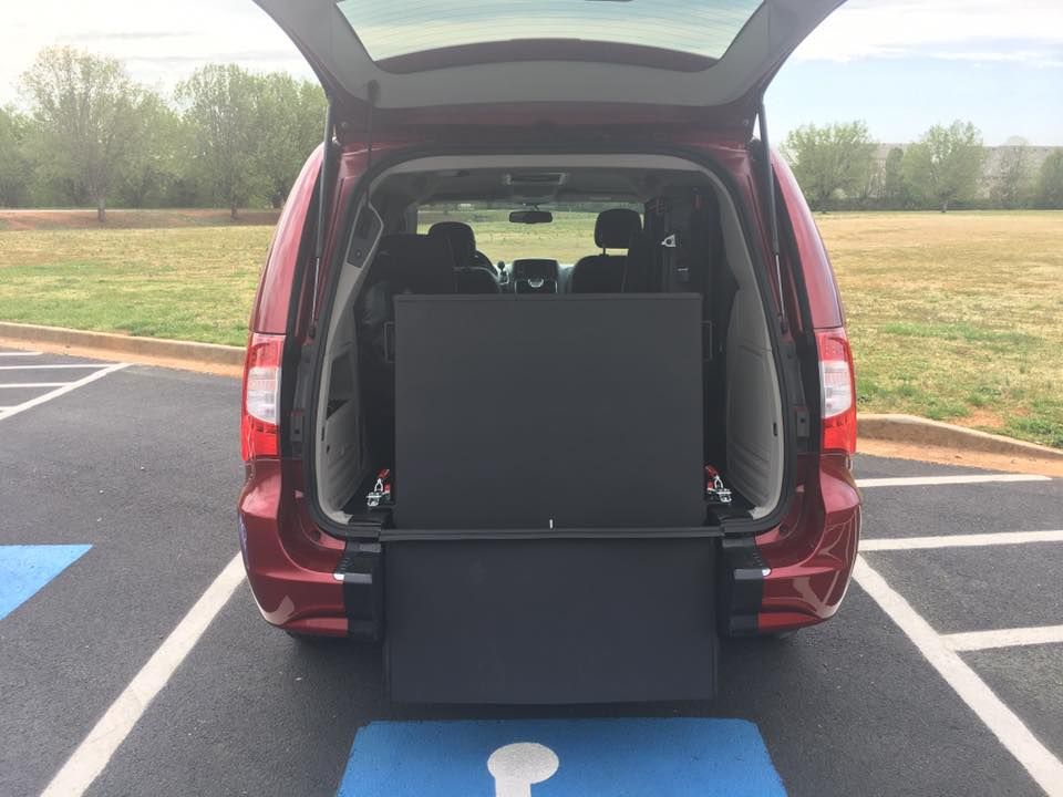 Red van with open trunk and wheelchair lift. Parked in a handicapped parking spot.