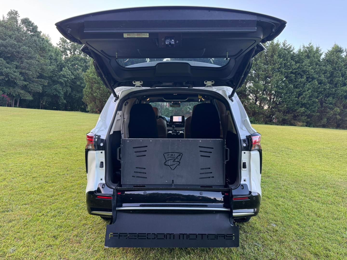 Rear view of a white SUV with open liftgate and ramp; Freedom Motors logo visible.