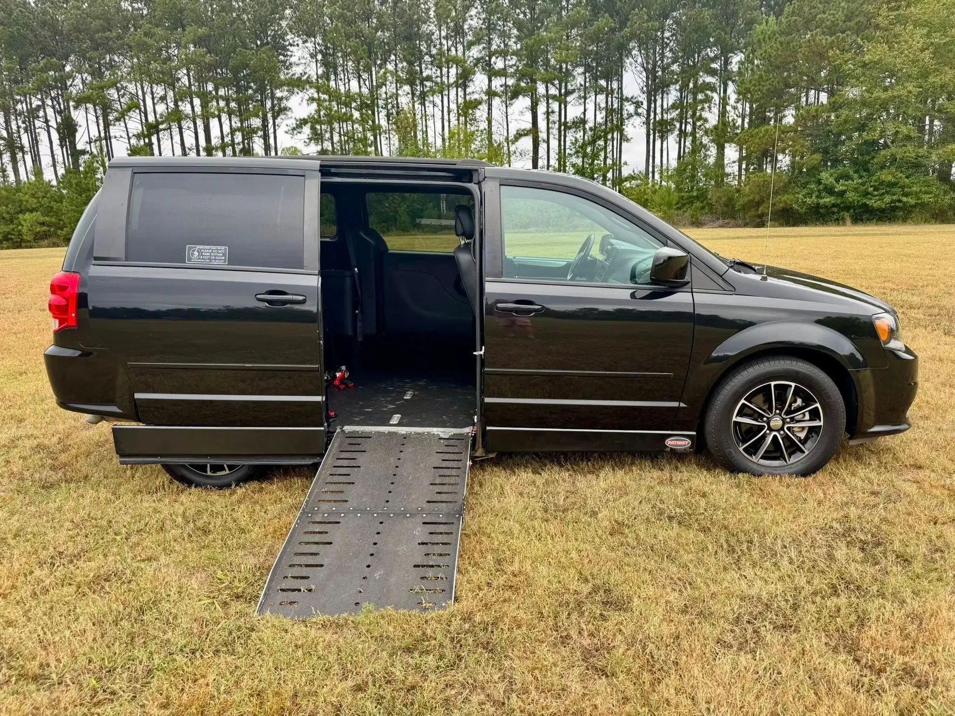 Black wheelchair-accessible van with ramp extended on grassy field.